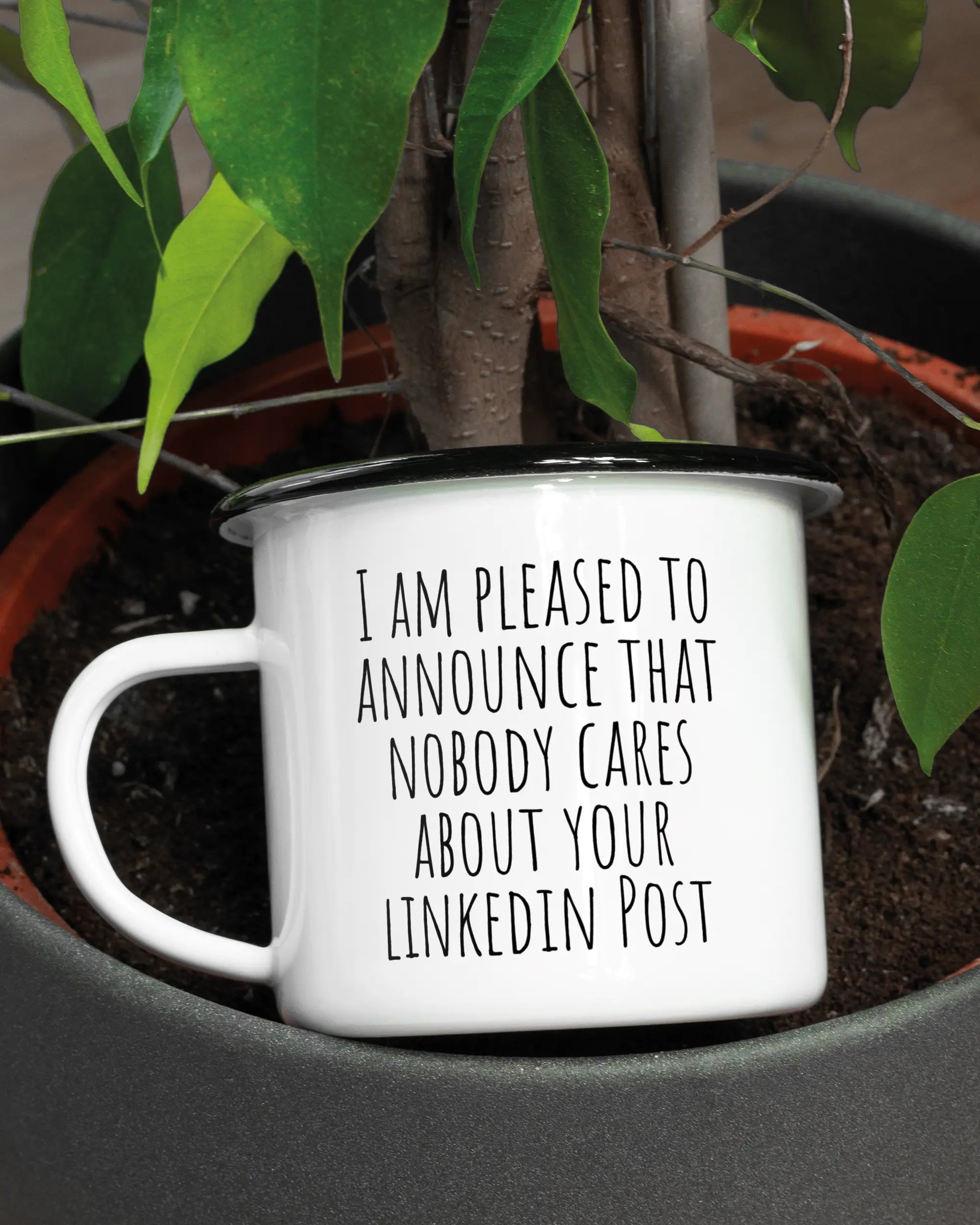 Aufnahme der linken Seite der beidseitig bedruckten Emailletasse von Maondo mit dem Design Please Unannounce in der Farbe White-Black in einem Blumentopf