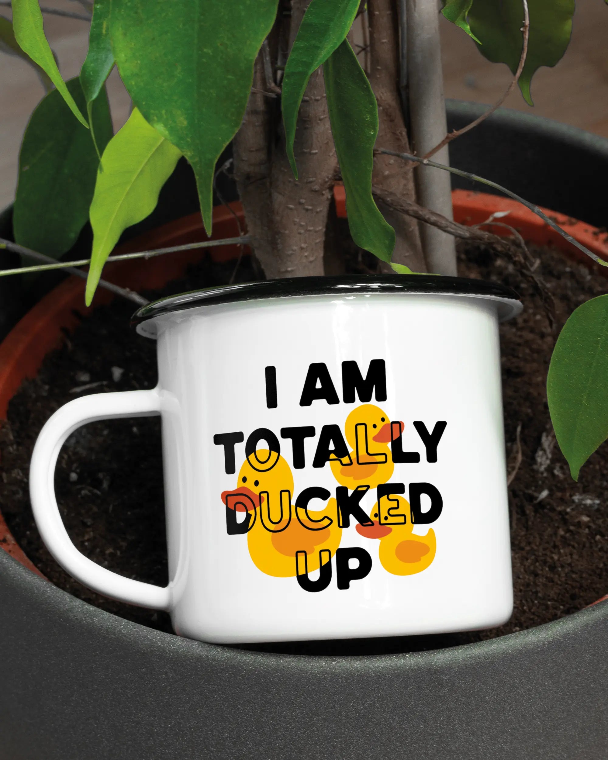 Aufnahme der linken Seite der beidseitig bedruckten Emailletasse von Maondo mit dem Design Ducked Up in der Farbe White-Black in einem Blumentopf