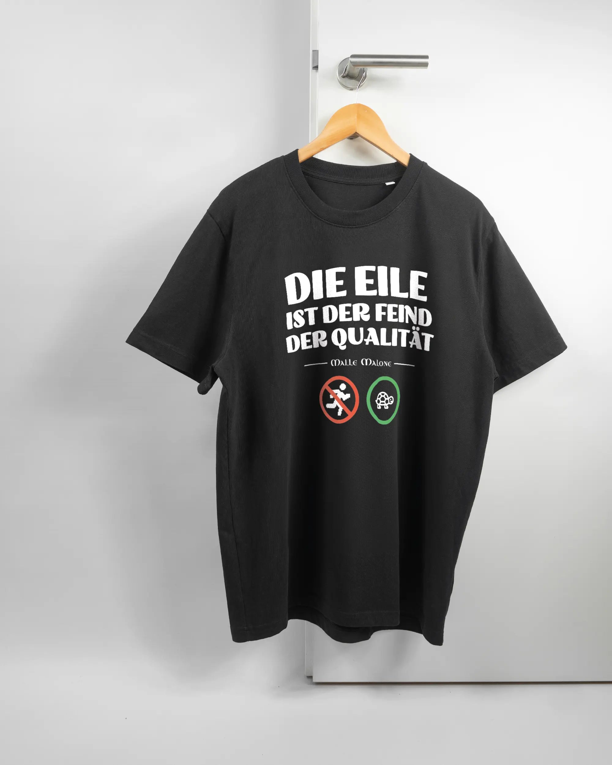 Vorderseite des Organic Unisex T-Shirt Relaxed von Maondo mit dem Design Keine Eile in der Farbe Black und in der Größe L auf einem Bügel an der Türklinke aufgehängt