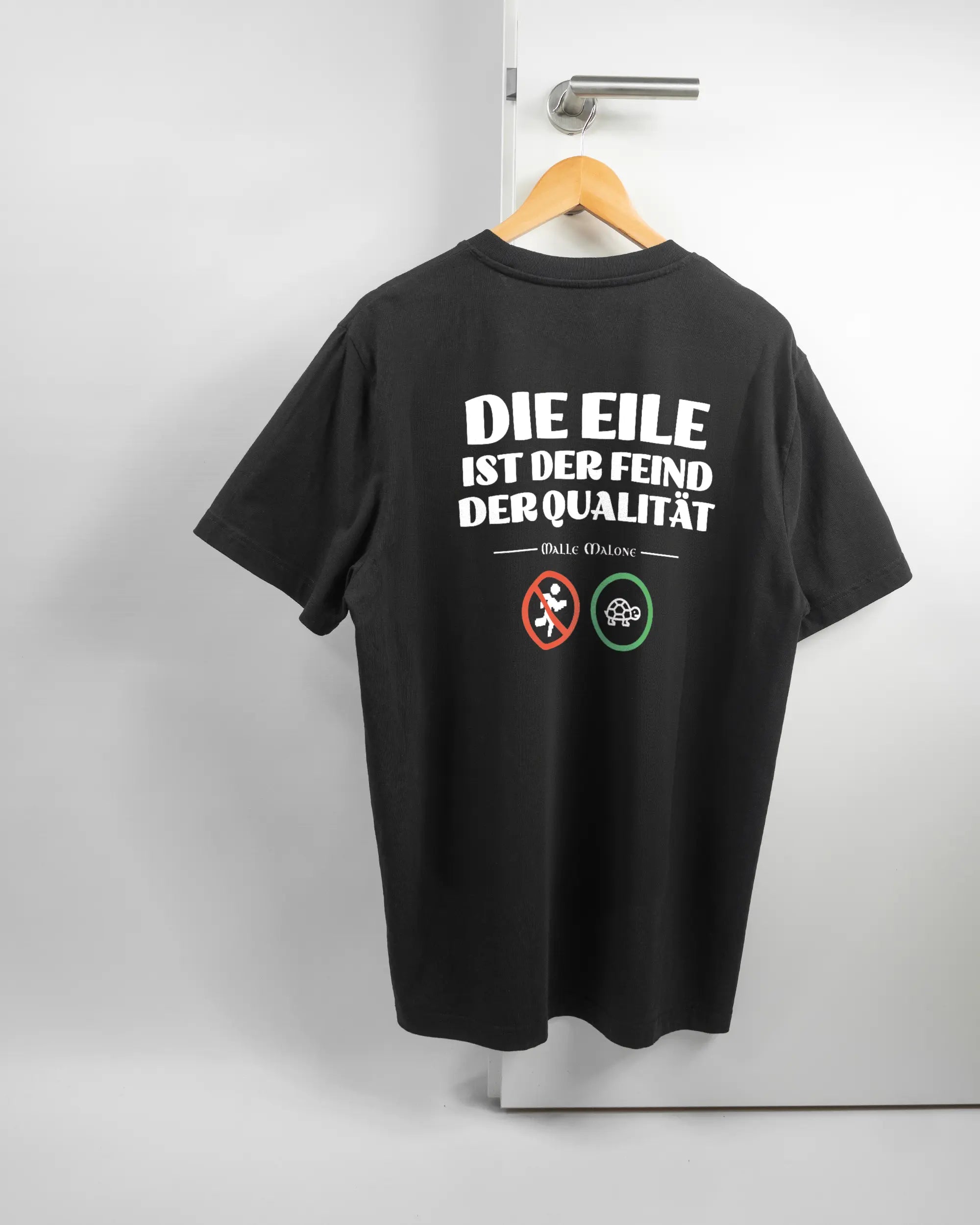 Rückseite des Organic Unisex T-Shirt Relaxed von Maondo mit dem Design Keine Eile in der Farbe Black und in der Größe L auf einem Bügel an der Türklinke aufgehängt