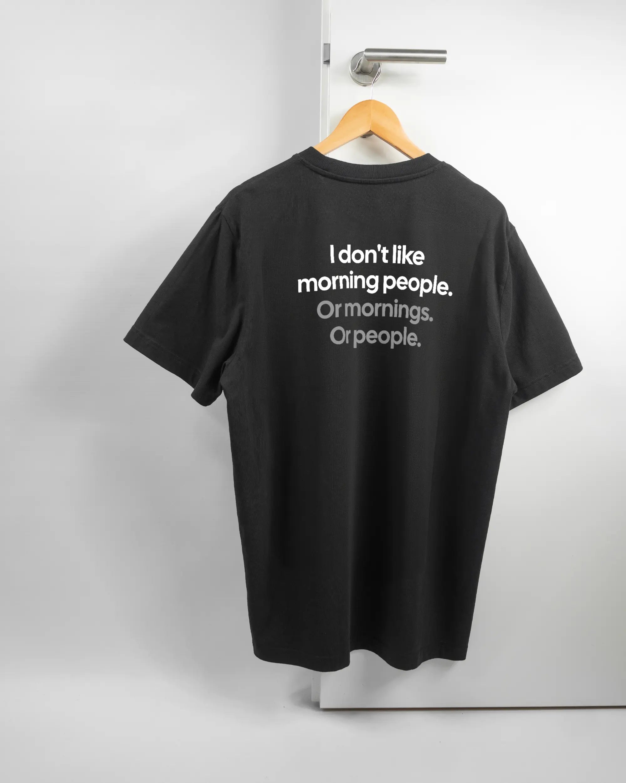Rückseite des Organic Unisex T-Shirt Relaxed von Maondo mit dem Design Morning Person in der Farbe Black und in der Größe L auf einem Bügel an der Türklinke aufgehängt