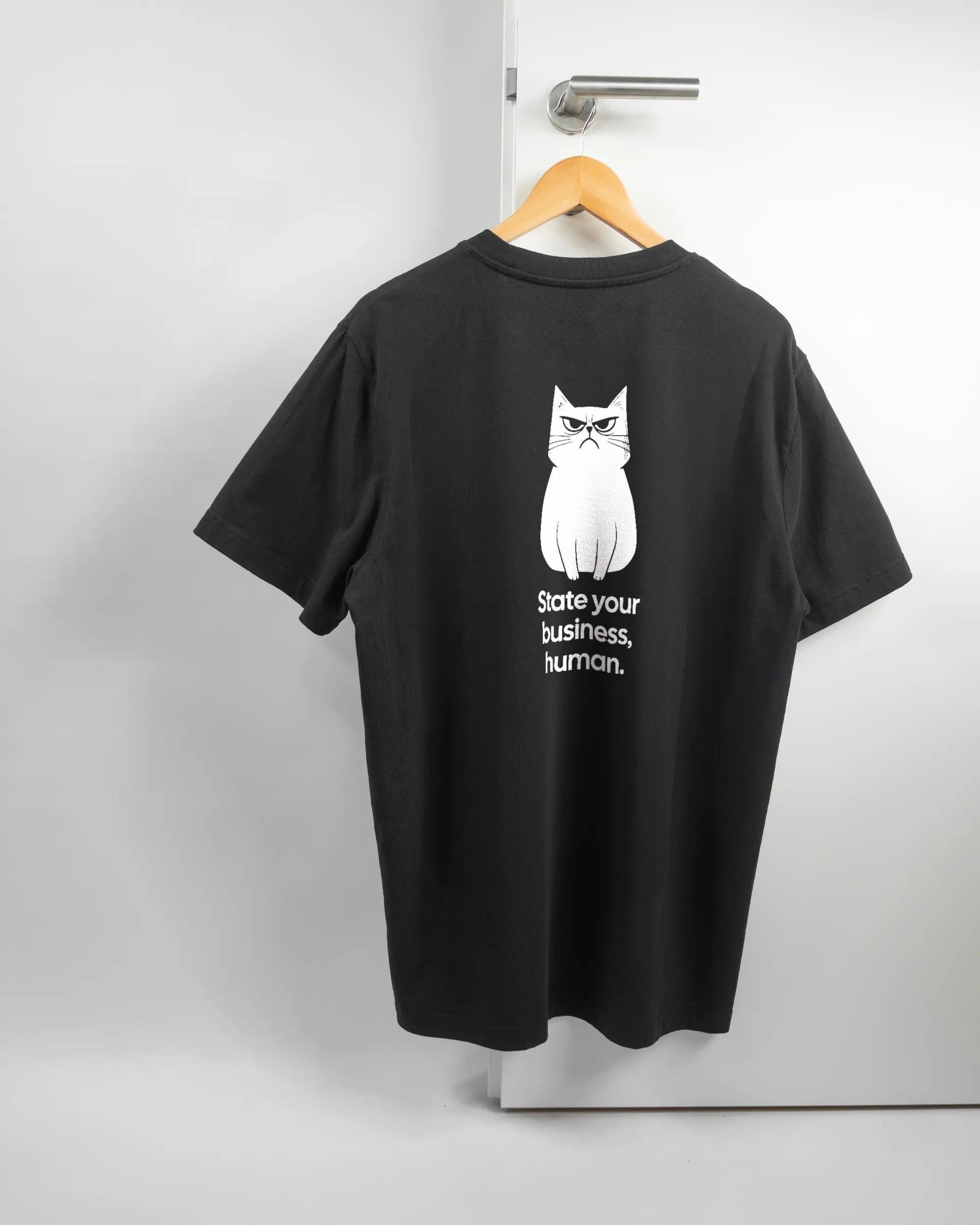 Rückseite des Organic Unisex T-Shirt Relaxed von Maondo mit dem Design Grumpy Purr in der Farbe Black und in der Größe L auf einem Bügel an der Türklinke aufgehängt