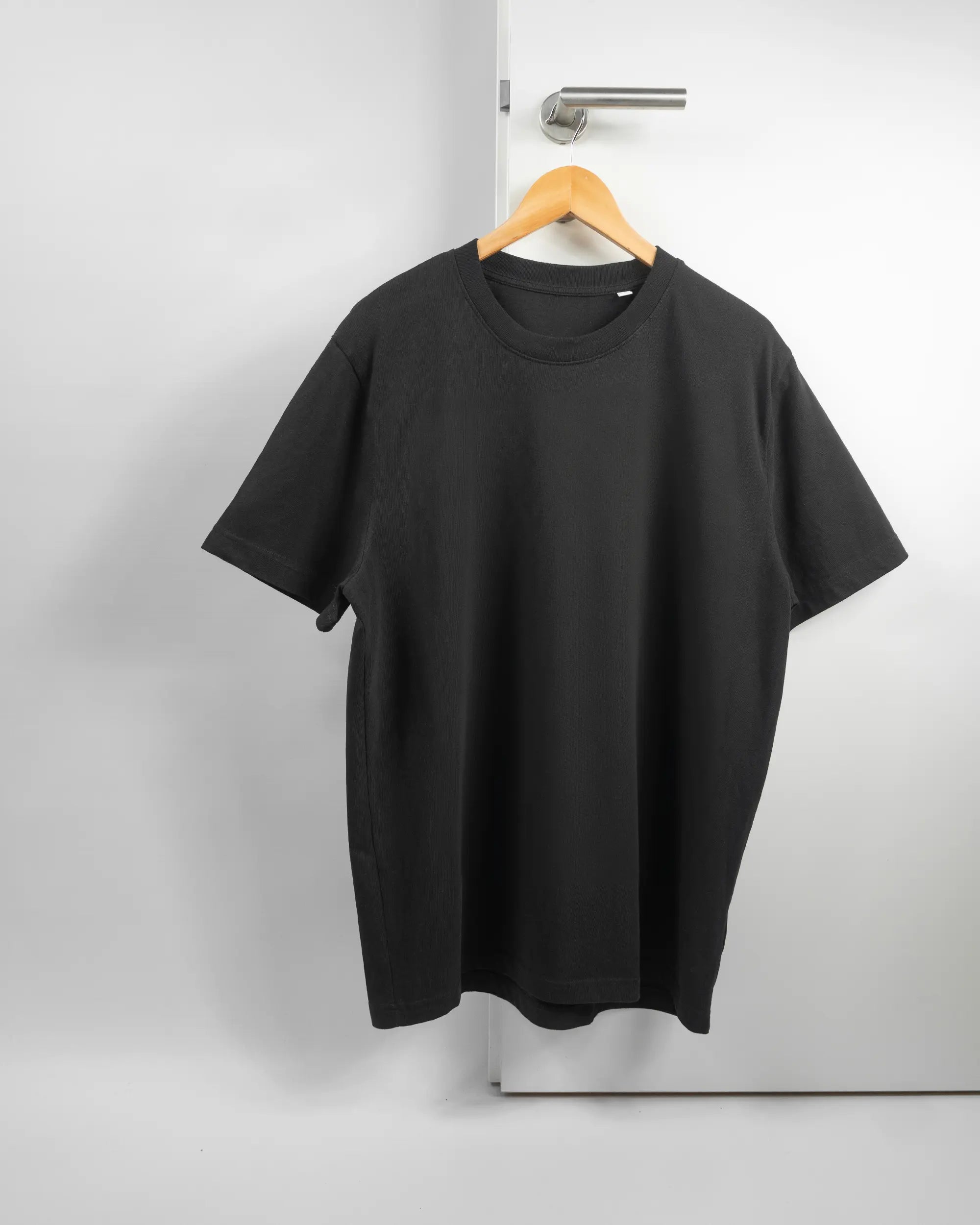 Vorderseite des Organic Unisex T-Shirt Relaxed von Maondo ohne Motiv in der Farbe Black und in der Größe L auf einem Bügel an der Türklinke aufgehängt