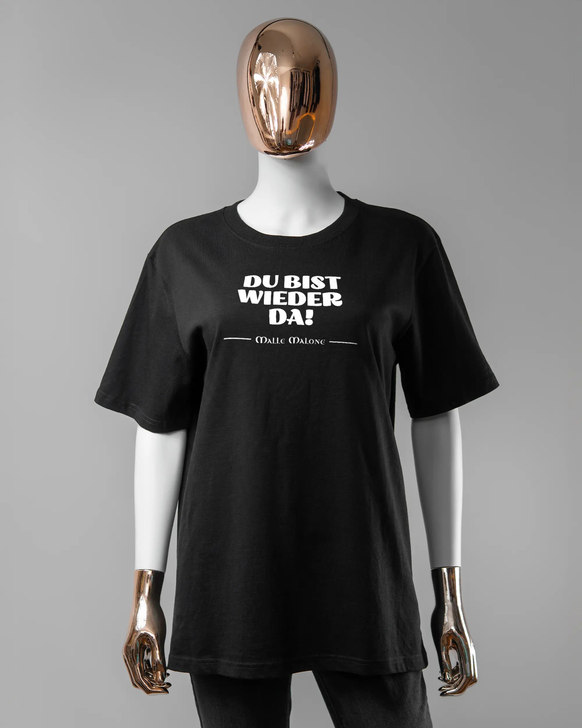 Vorderseite des Organic Unisex T-Shirt Relaxed von Maondo mit dem Design Wieder da in der Farbe Black und in der Größe S getragen von einer femininen Puppe