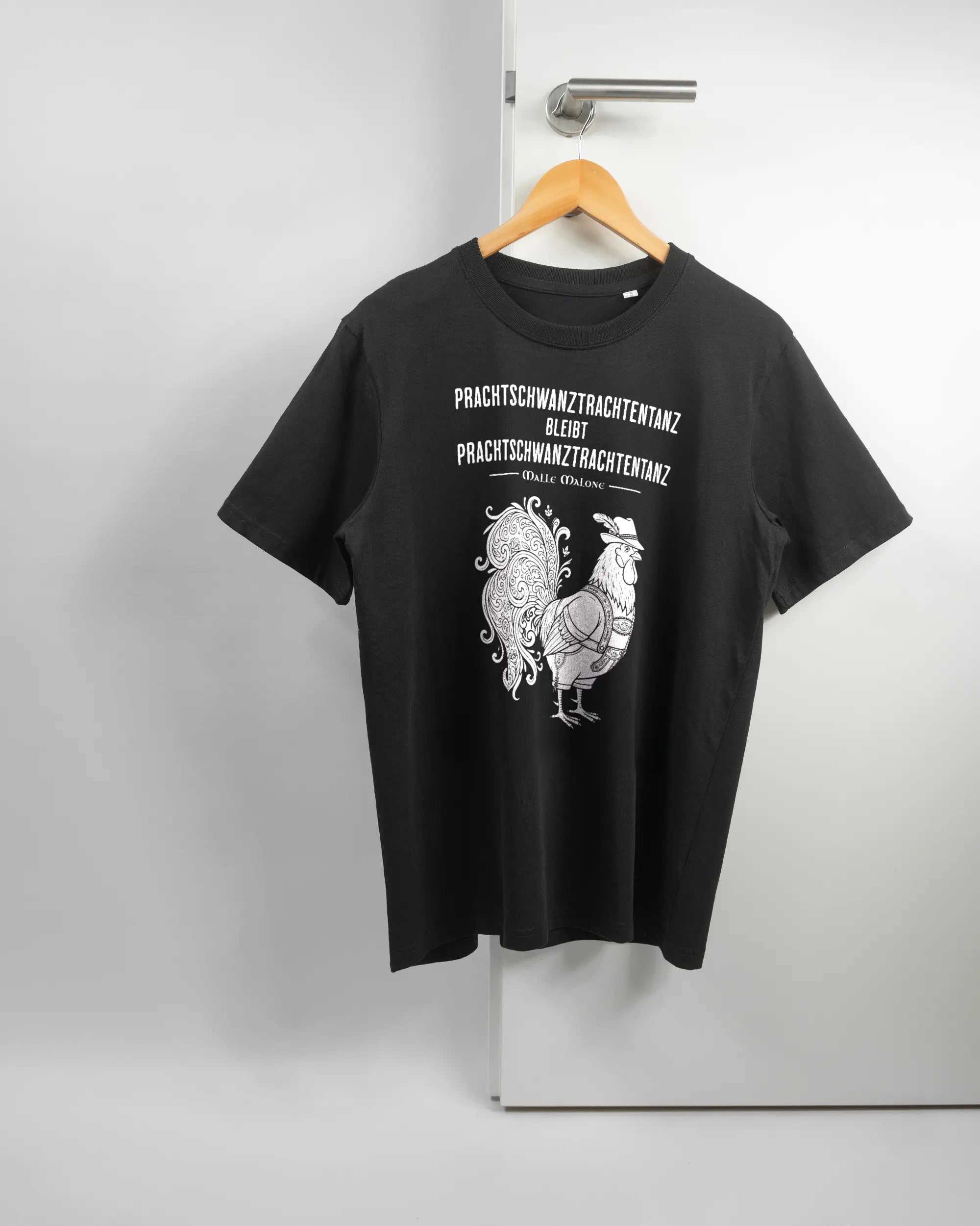 Vorderseite des Organic Unisex T-Shirt Relaxed von Maondo mit dem Design Trachtentanz in der Farbe Black und in der Größe S auf einem Bügel an der Türklinke aufgehängt
