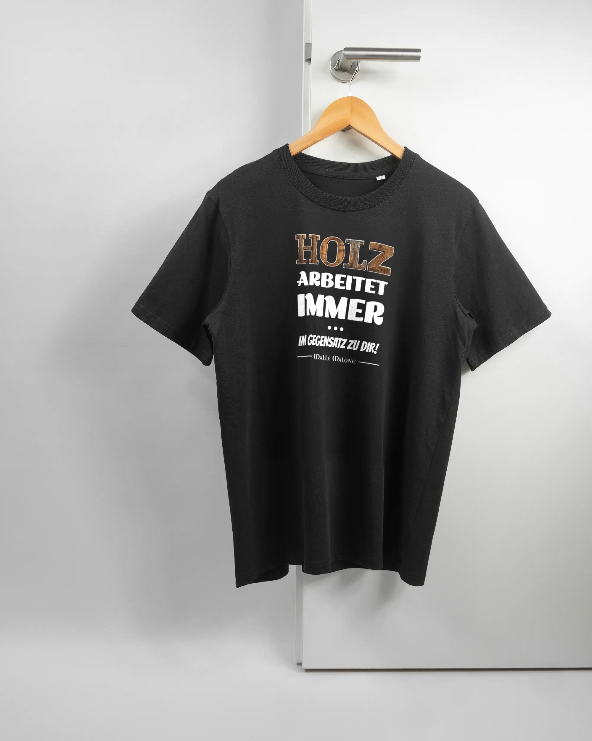 Vorderseite des Organic Unisex T-Shirt Relaxed von Maondo mit dem Design Holzarbeit in der Farbe Black und in der Größe S auf einem Bügel an der Türklinke aufgehängt