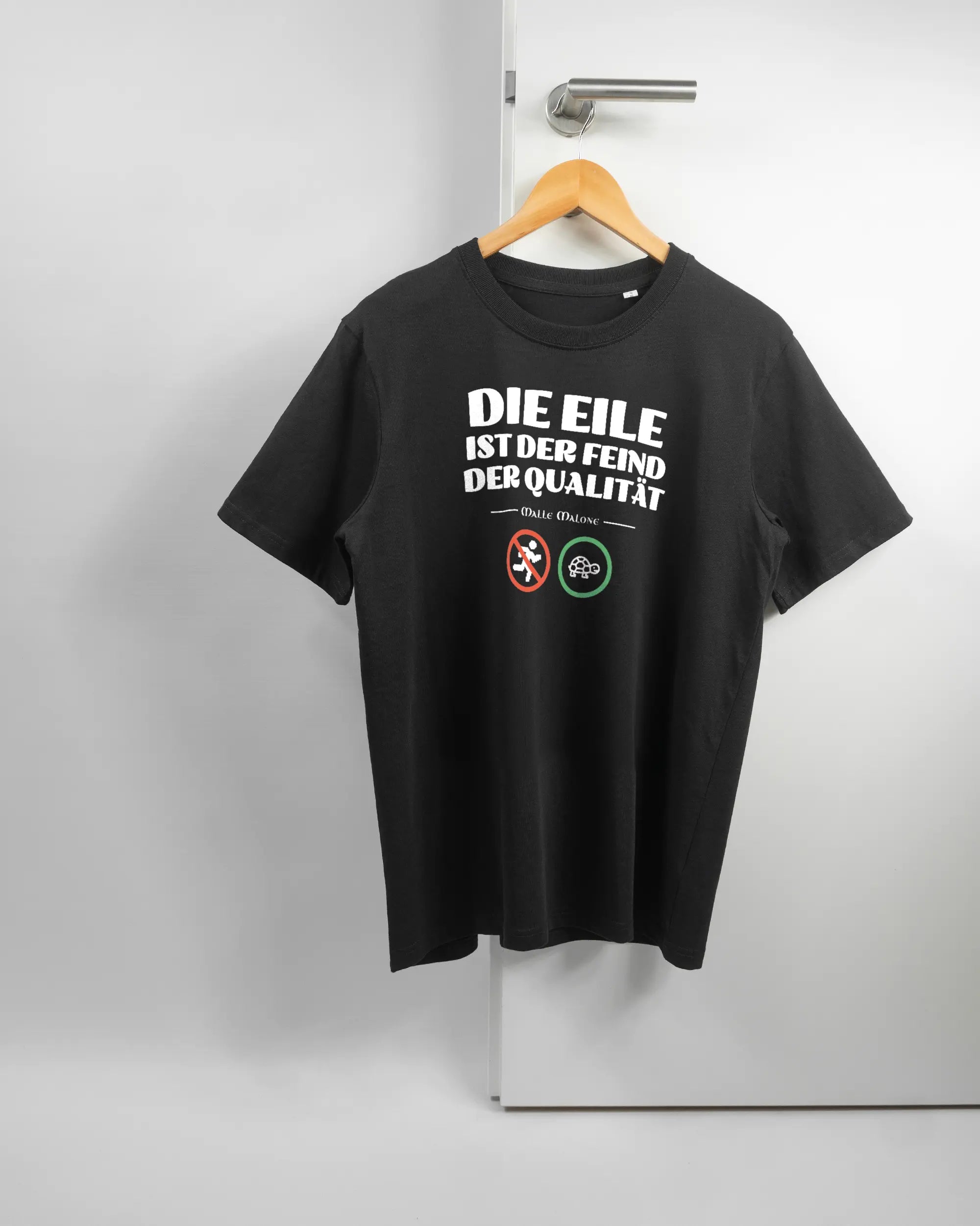 Vorderseite des Organic Unisex T-Shirt Relaxed von Maondo mit dem Design Keine Eile in der Farbe Black und in der Größe S auf einem Bügel an der Türklinke aufgehängt