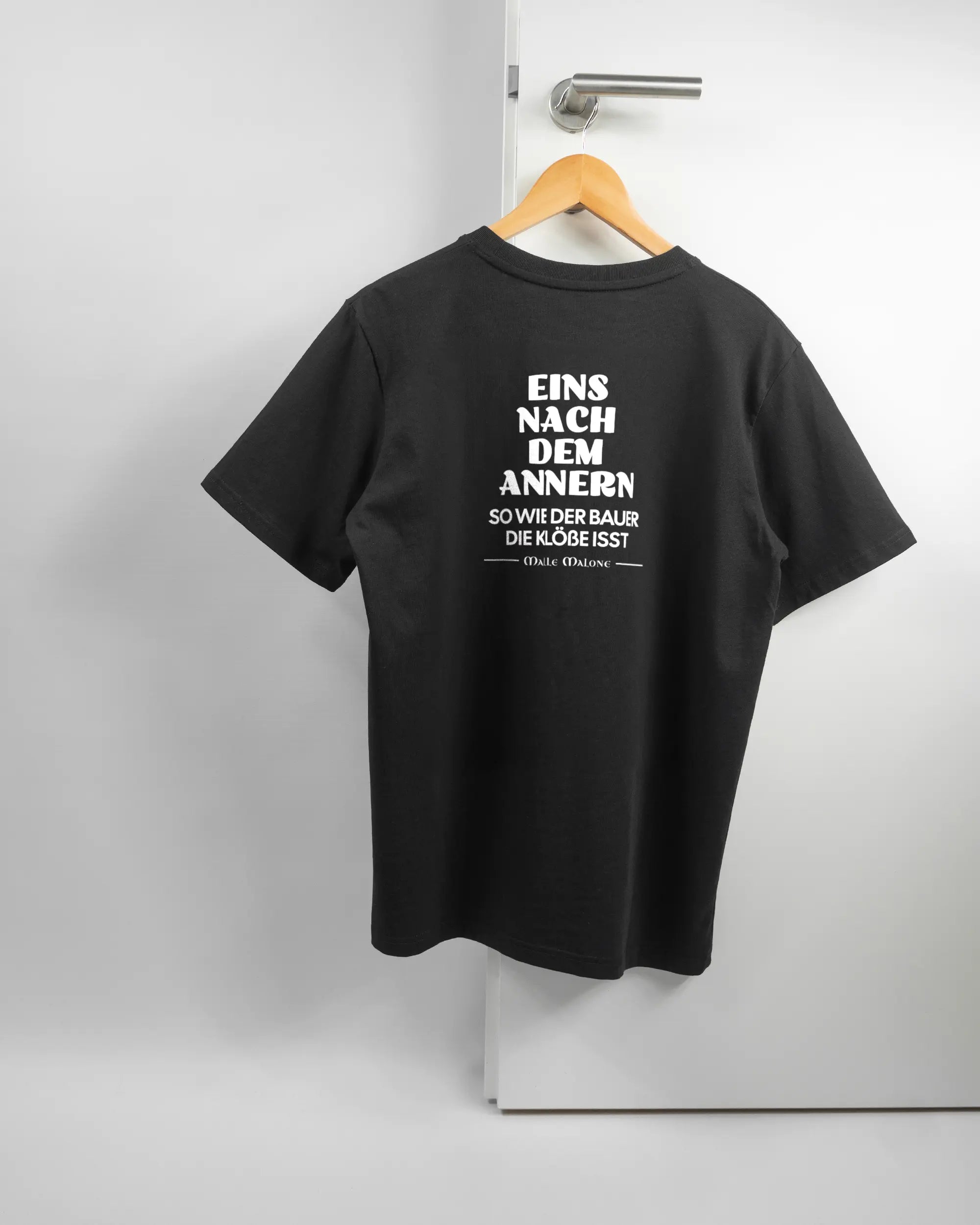 Rückseite des Organic Unisex T-Shirt Relaxed von Maondo mit dem Design Eins nach dem Annern in der Farbe Black und in der Größe S auf einem Bügel an der Türklinke aufgehängt