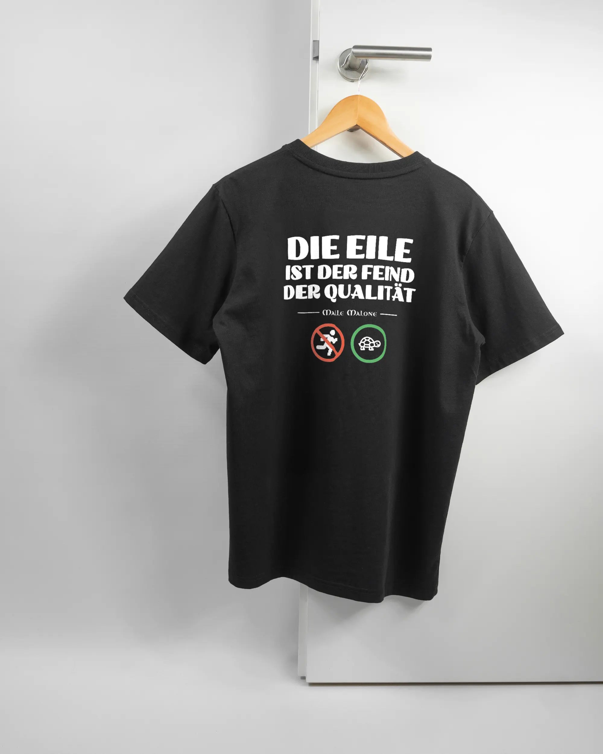 Rückseite des Organic Unisex T-Shirt Relaxed von Maondo mit dem Design Keine Eile in der Farbe Black und in der Größe S auf einem Bügel an der Türklinke aufgehängt