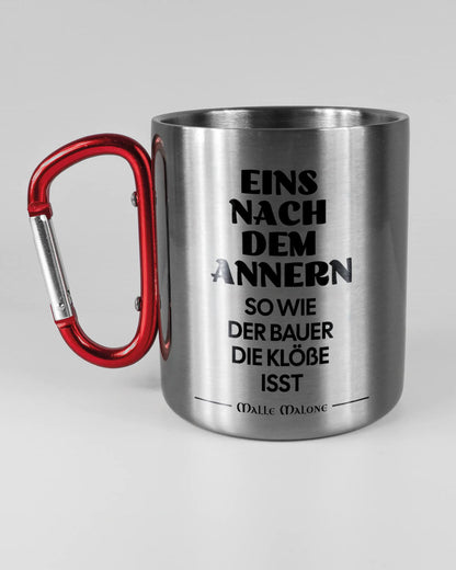 Titelbild, das die linke Seite der beidseitig bedruckten Edelstahltasse von Maondo mit dem Design Eins nach dem Annern in der Farbe Metallic-Red auf einem Holztisch zeigt