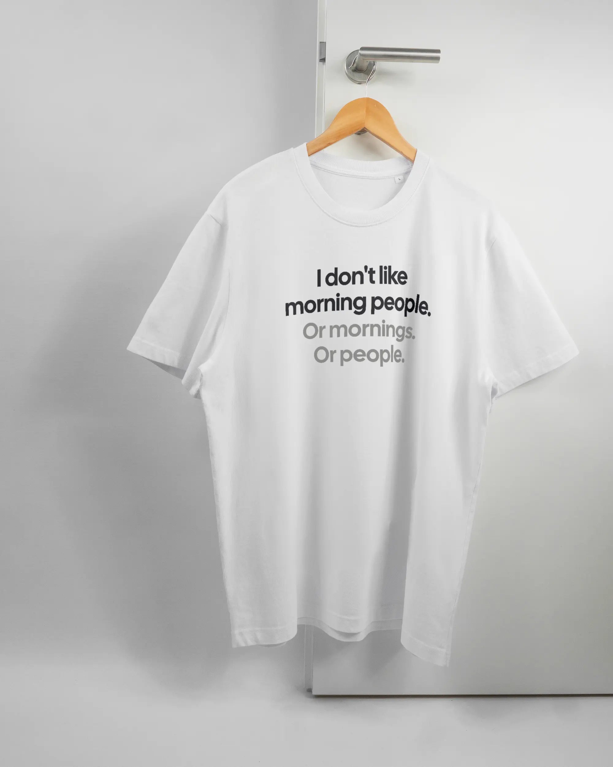 Vorderseite des Organic Unisex T-Shirt Relaxed von Maondo mit dem Design Morning Person in der Farbe White und in der Größe L auf einem Bügel an der Türklinke aufgehängt