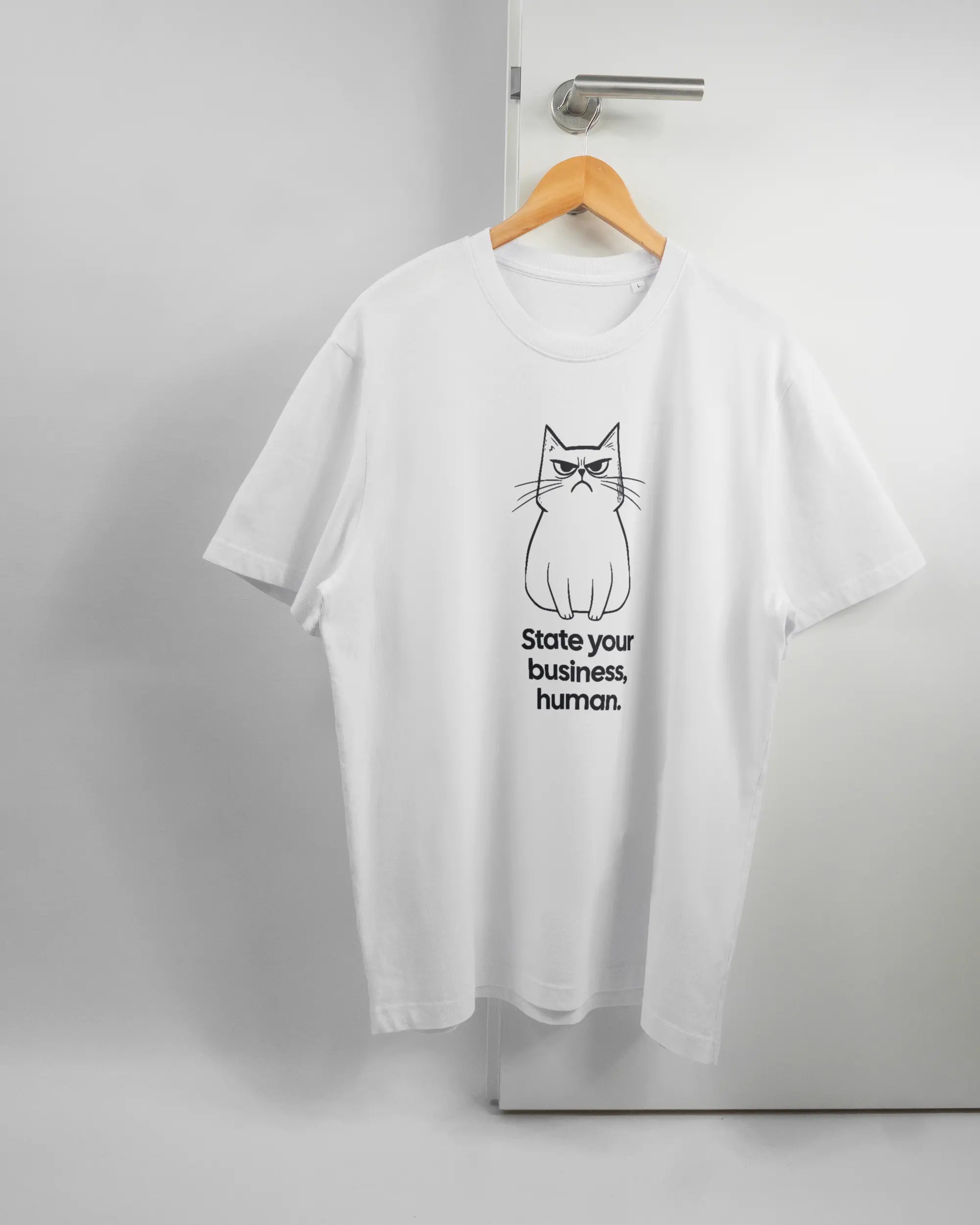 Vorderseite des Organic Unisex T-Shirt Relaxed von Maondo mit dem Design Grumpy Purr in der Farbe White und in der Größe L auf einem Bügel an der Türklinke aufgehängt