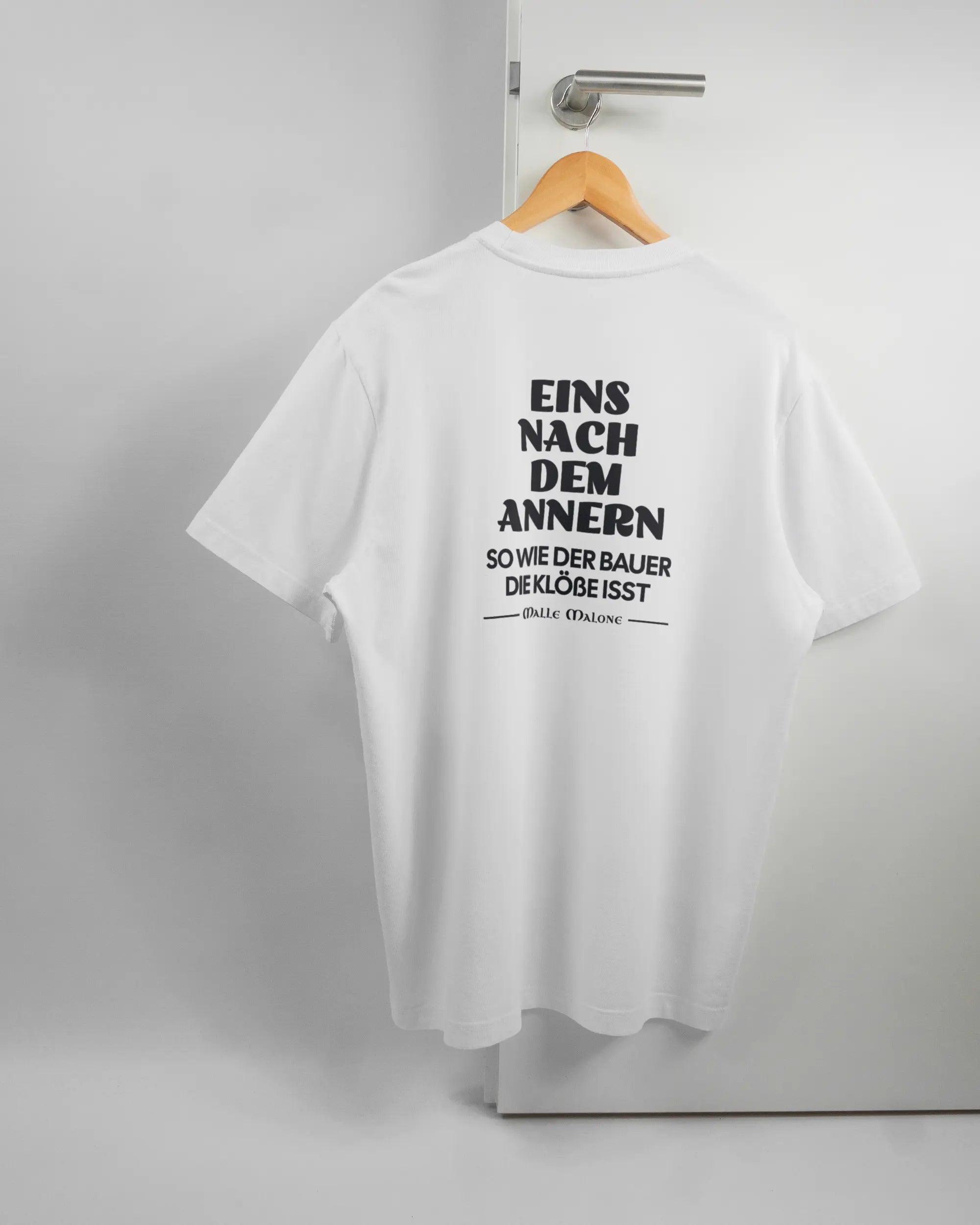 Rückseite des Organic Unisex T-Shirt Relaxed von Maondo mit dem Design Eins nach dem Annern in der Farbe White und in der Größe L auf einem Bügel an der Türklinke aufgehängt