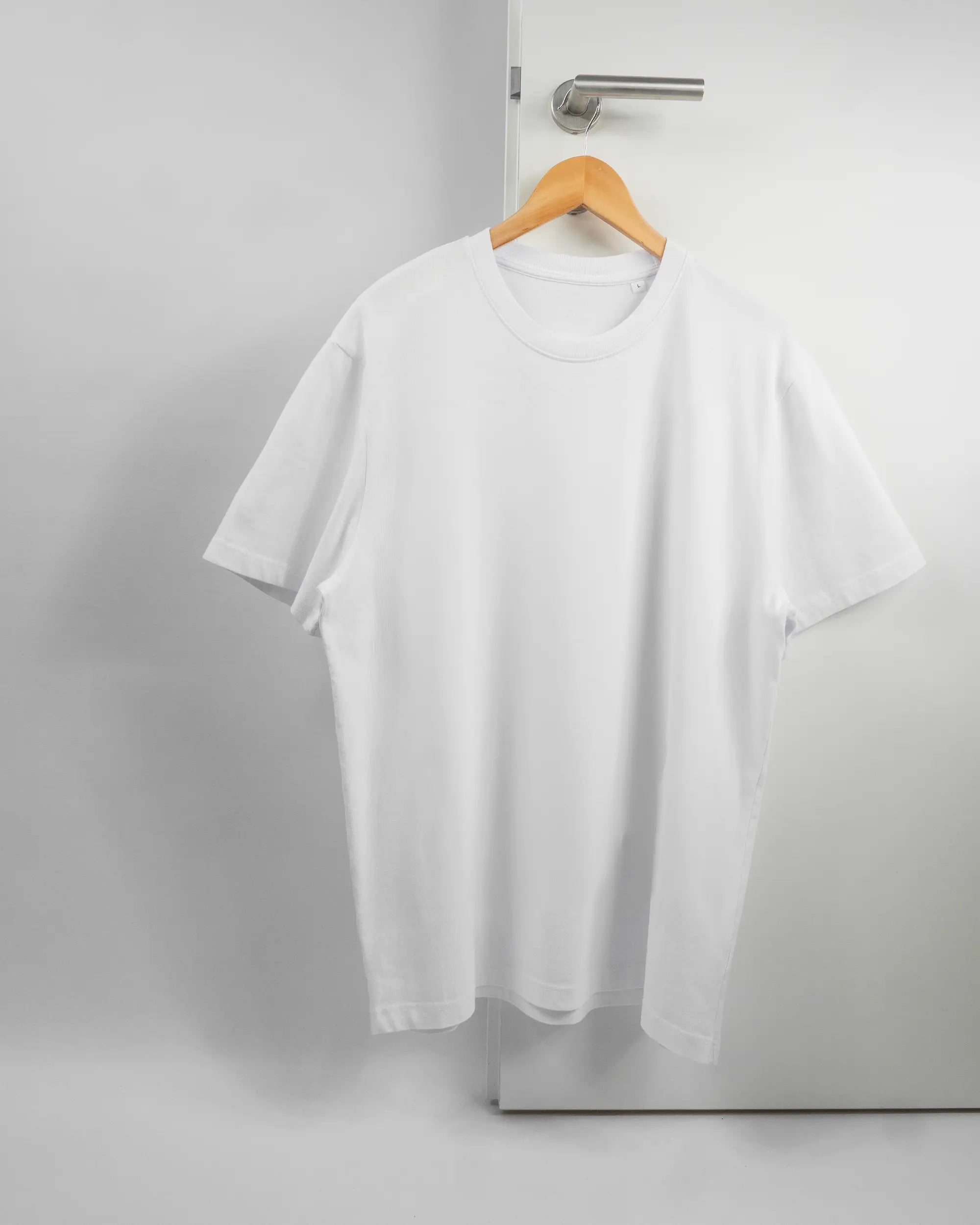 Vorderseite des Organic Unisex T-Shirt Relaxed von Maondo ohne Motiv in der Farbe White und in der Größe L auf einem Bügel an der Türklinke aufgehängt