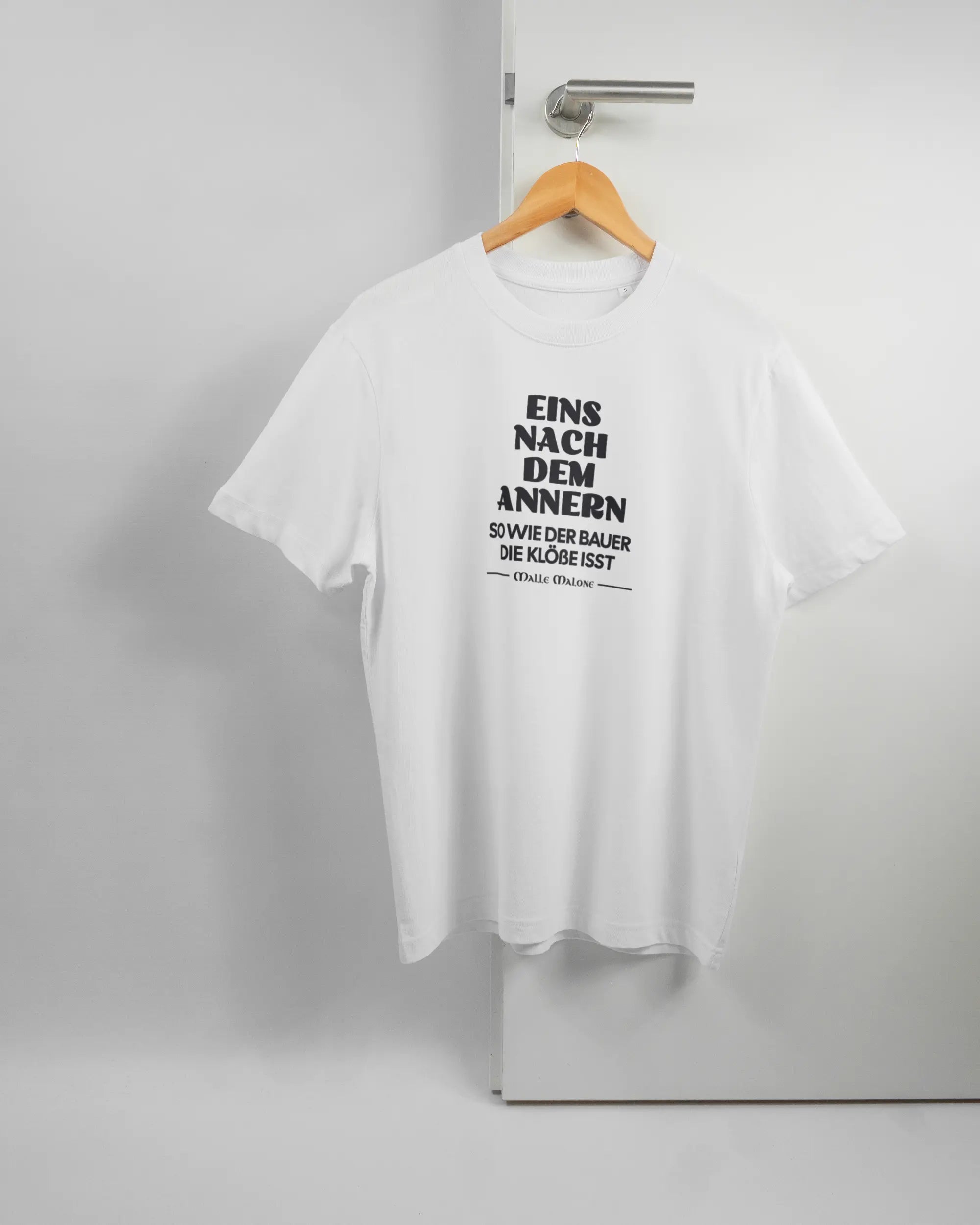 Vorderseite des Organic Unisex T-Shirt Relaxed von Maondo mit dem Design Eins nach dem Annern in der Farbe White und in der Größe S auf einem Bügel an der Türklinke aufgehängt