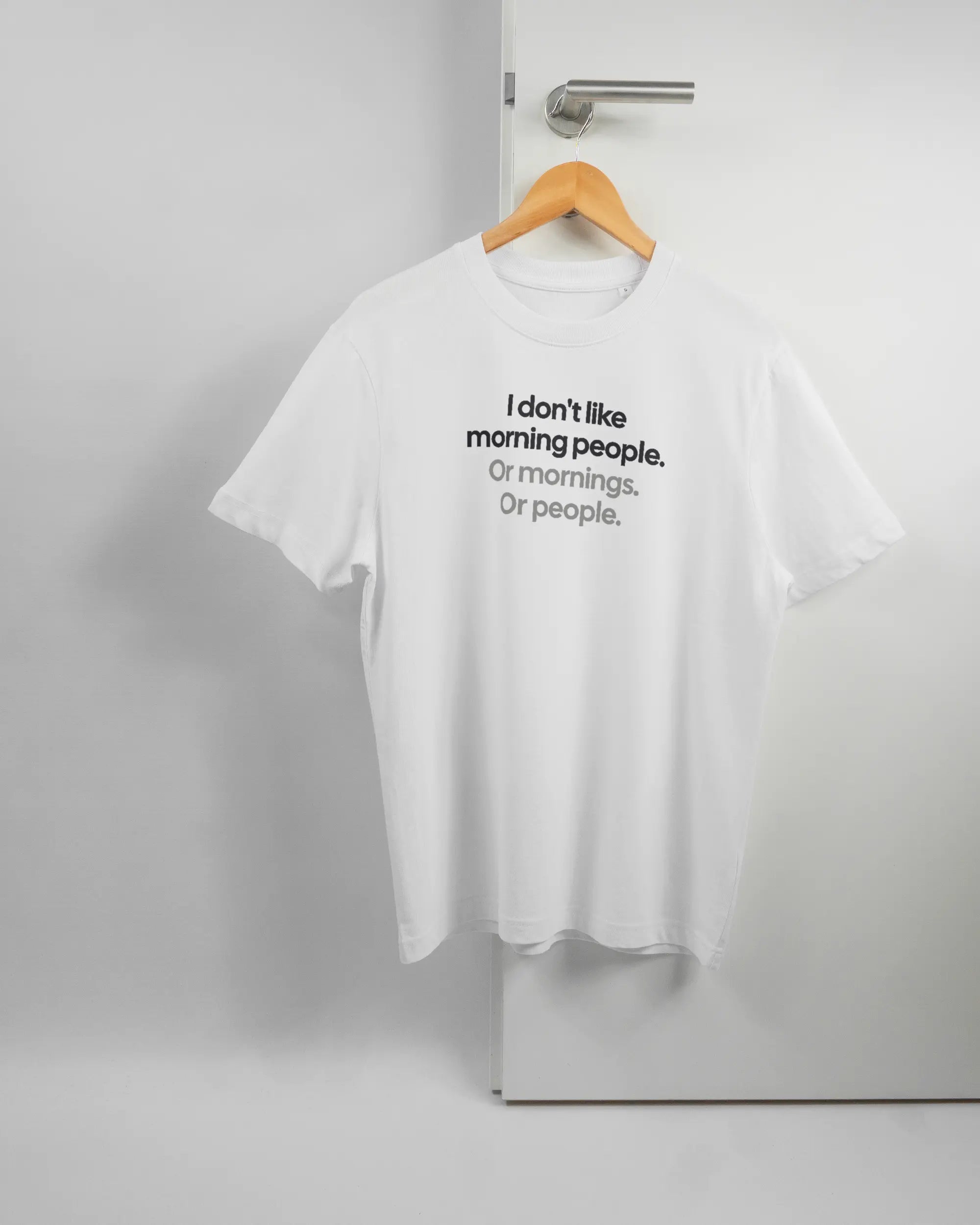 Vorderseite des Organic Unisex T-Shirt Relaxed von Maondo mit dem Design Morning Person in der Farbe White und in der Größe S auf einem Bügel an der Türklinke aufgehängt