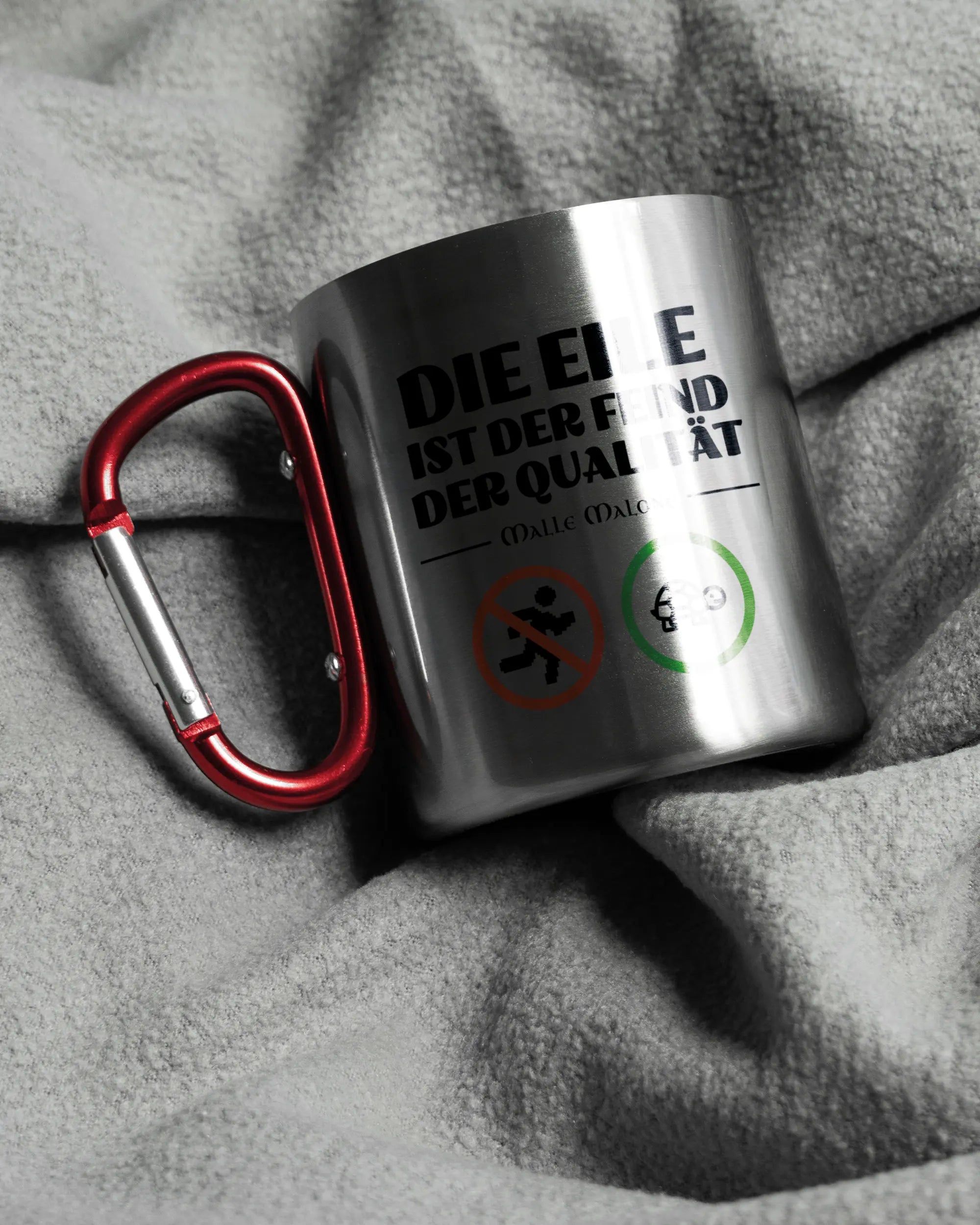 Aufnahme, die die linke Seite der beidseitig bedruckten Edelstahltasse von Maondo auf einer flauschigen Fließdecke mit dem Design Keine Eile in der Farbe Metallic-Red zeigt