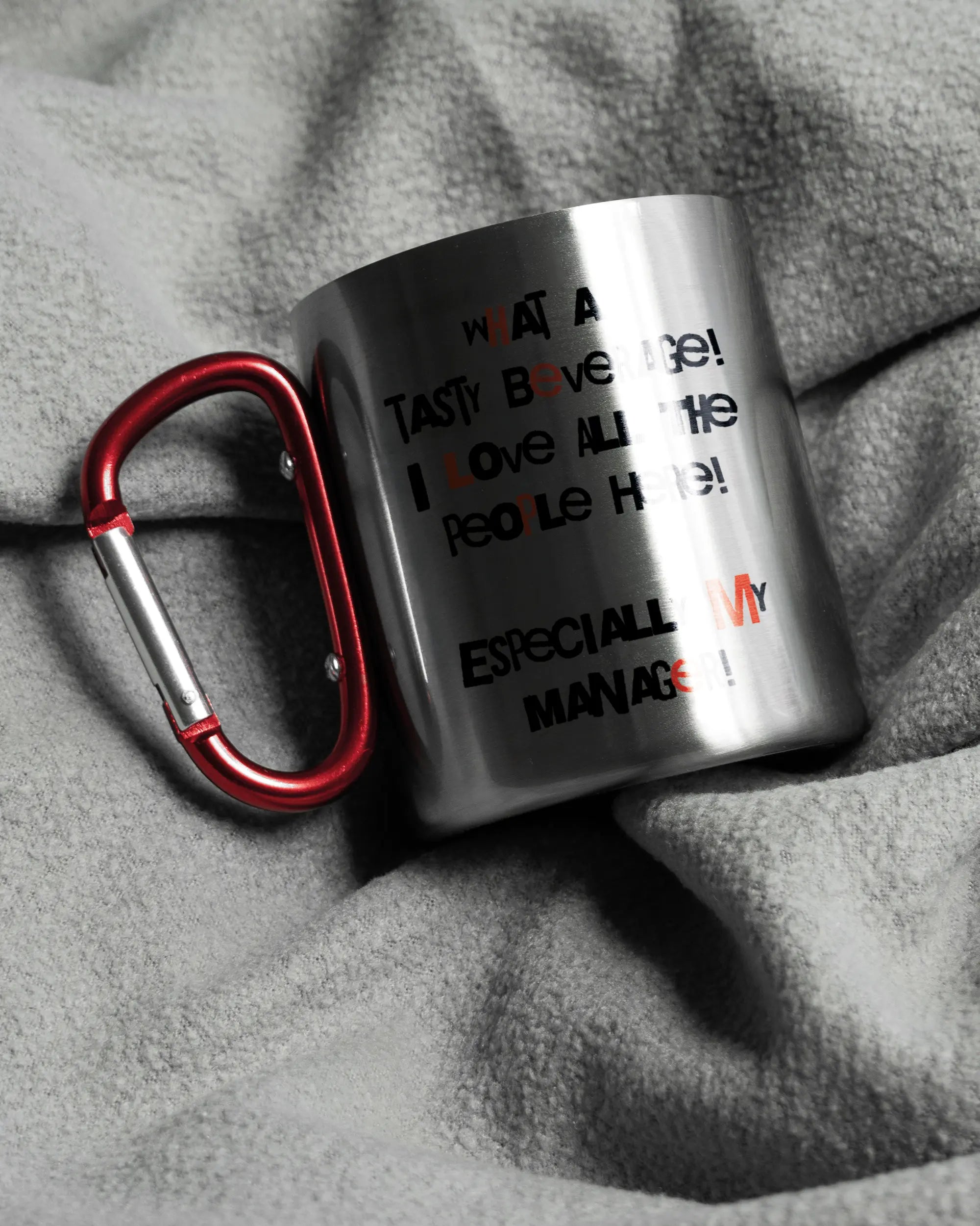 Aufnahme, die die linke Seite der beidseitig bedruckten Edelstahltasse von Maondo auf einer flauschigen Fließdecke mit dem Design Help me in der Farbe Metallic-Red zeigt