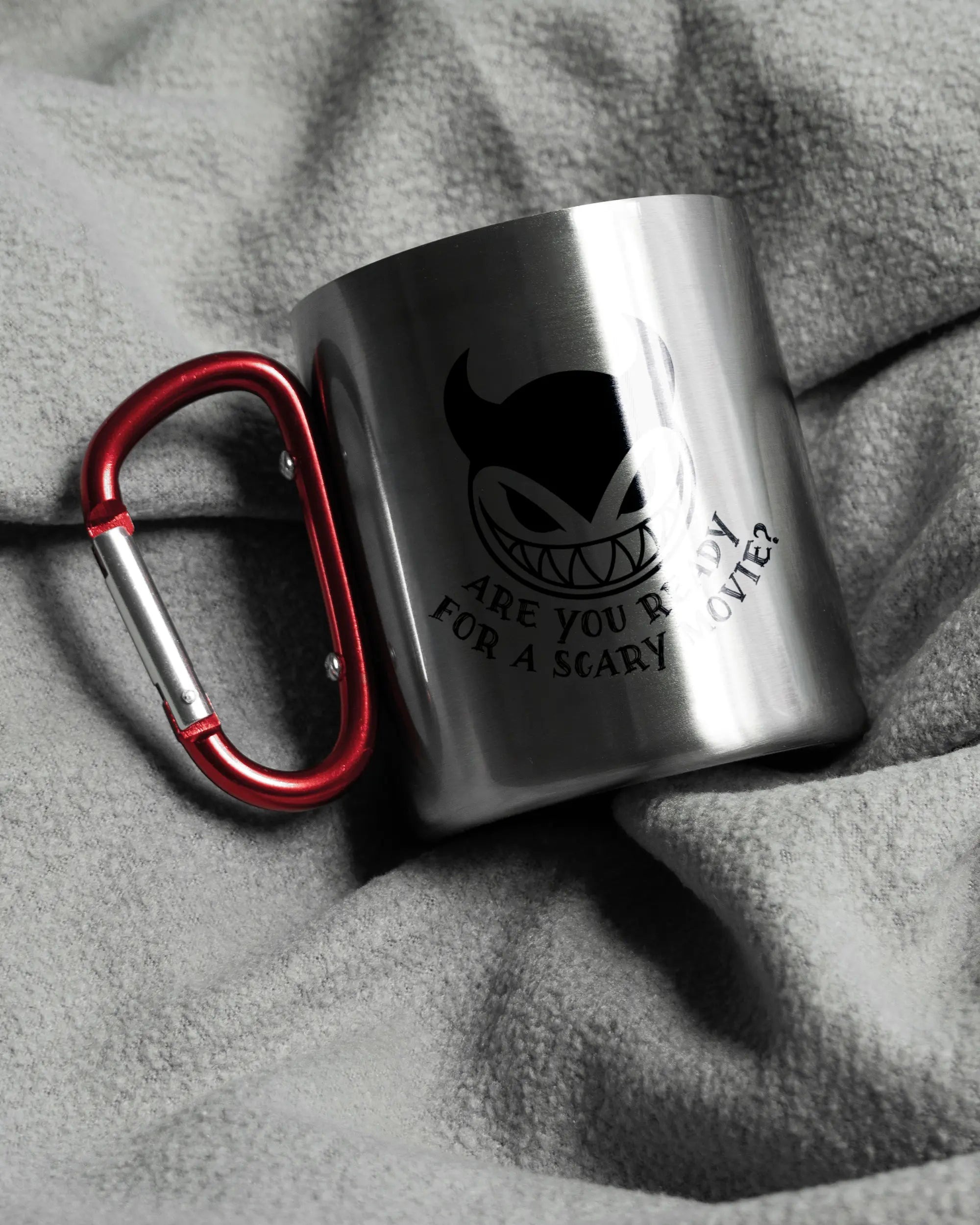 Aufnahme, die die linke Seite der beidseitig bedruckten Edelstahltasse von Maondo auf einer flauschigen Fließdecke mit dem Design Scary Movie in der Farbe Metallic-Red zeigt