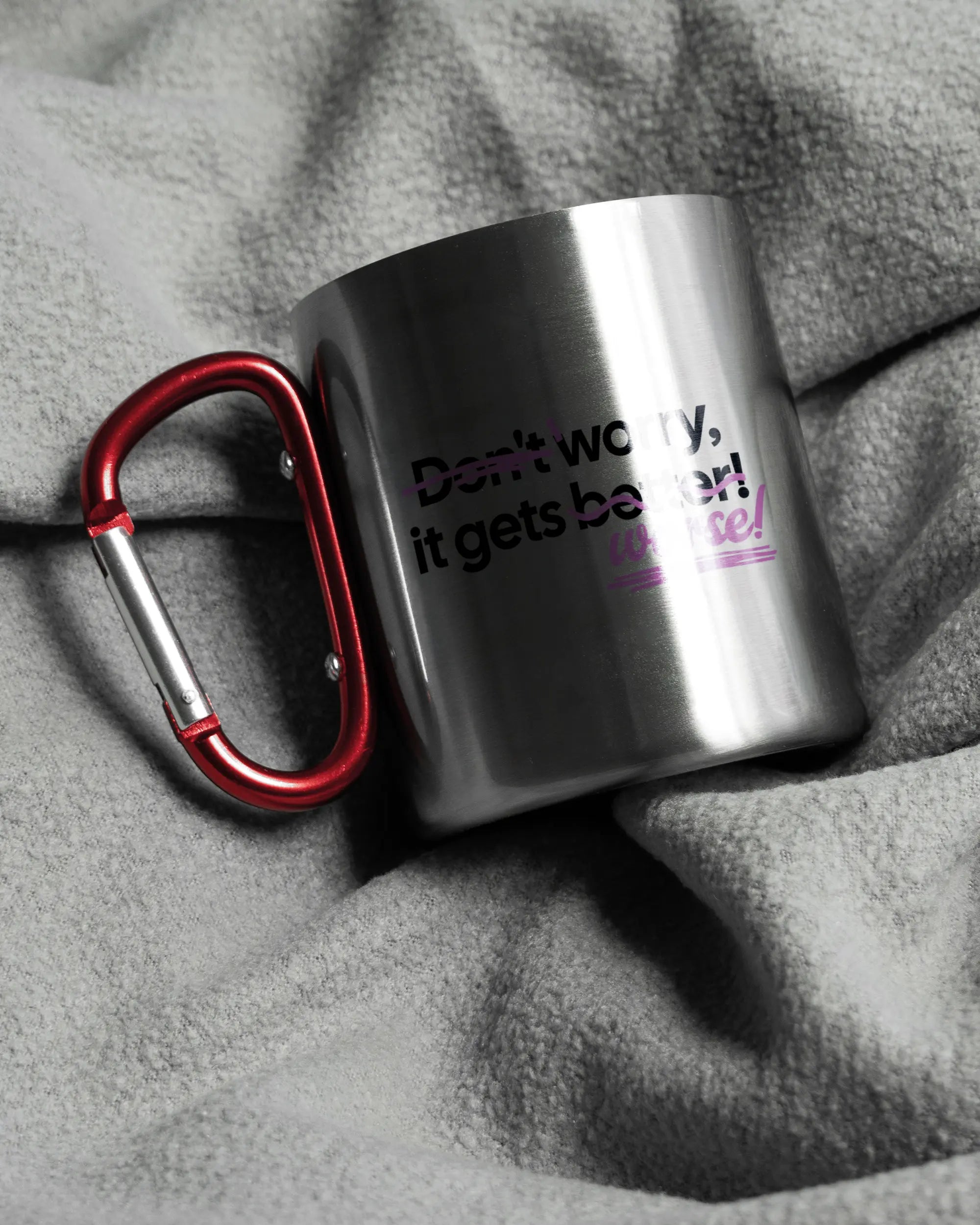 Aufnahme, die die linke Seite der beidseitig bedruckten Edelstahltasse von Maondo auf einer flauschigen Fließdecke mit dem Design Worry Worse in der Farbe Metallic-Red zeigt
