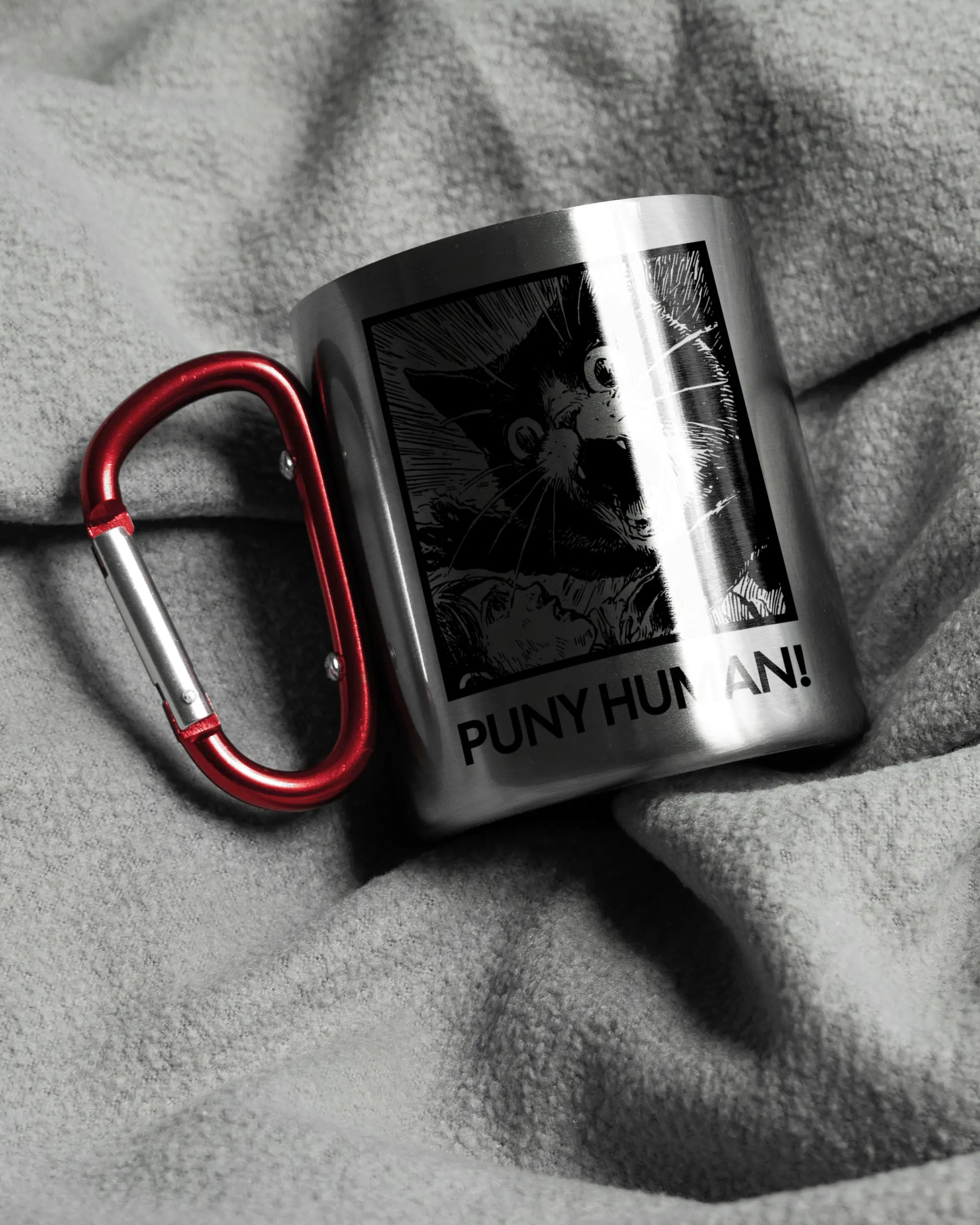 Aufnahme, die die linke Seite der beidseitig bedruckten Edelstahltasse von Maondo auf einer flauschigen Fließdecke mit dem Design Puny Human in der Farbe Metallic-Red zeigt