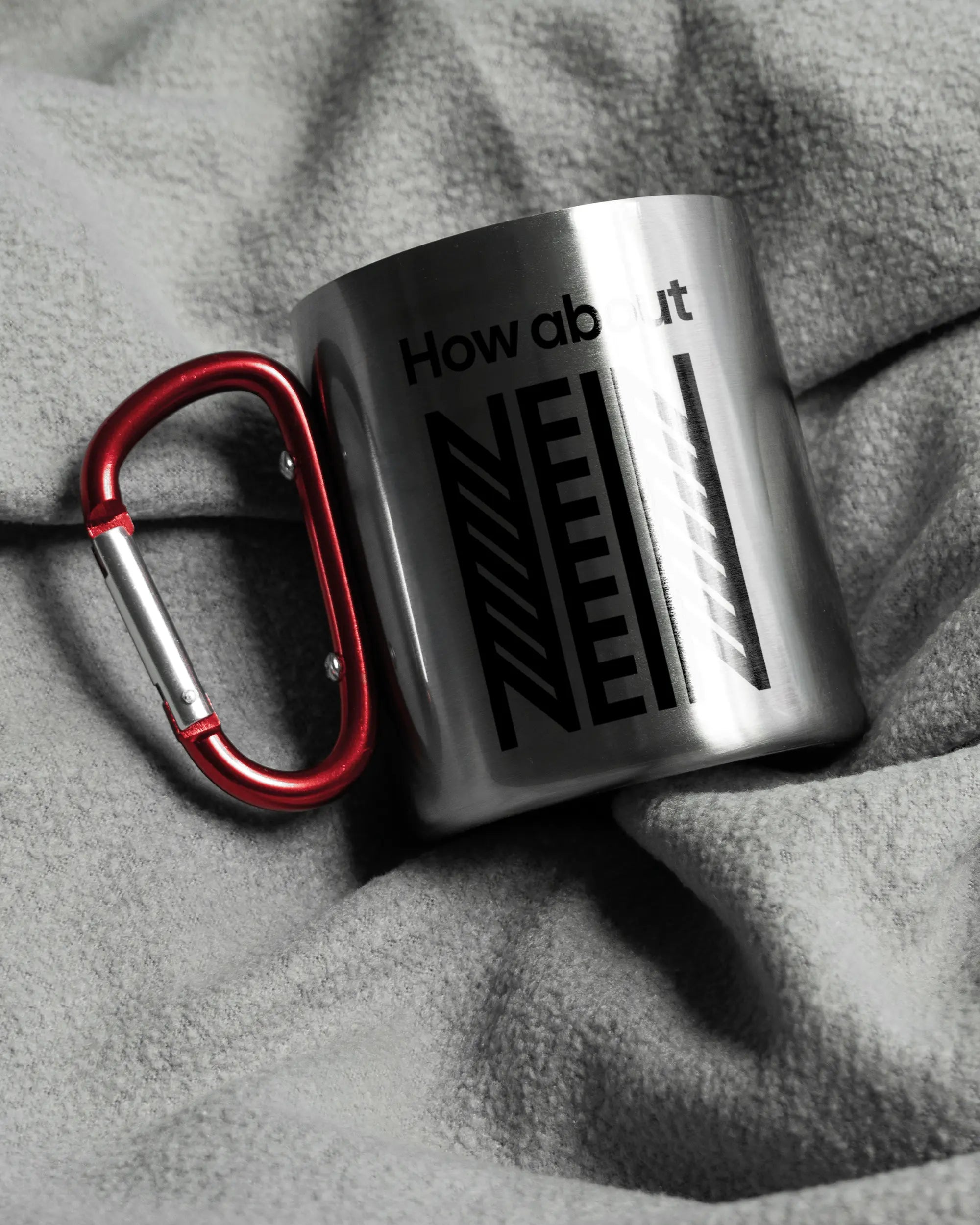 Aufnahme, die die linke Seite der beidseitig bedruckten Edelstahltasse von Maondo auf einer flauschigen Fließdecke mit dem Design How about nein in der Farbe Metallic-Red zeigt