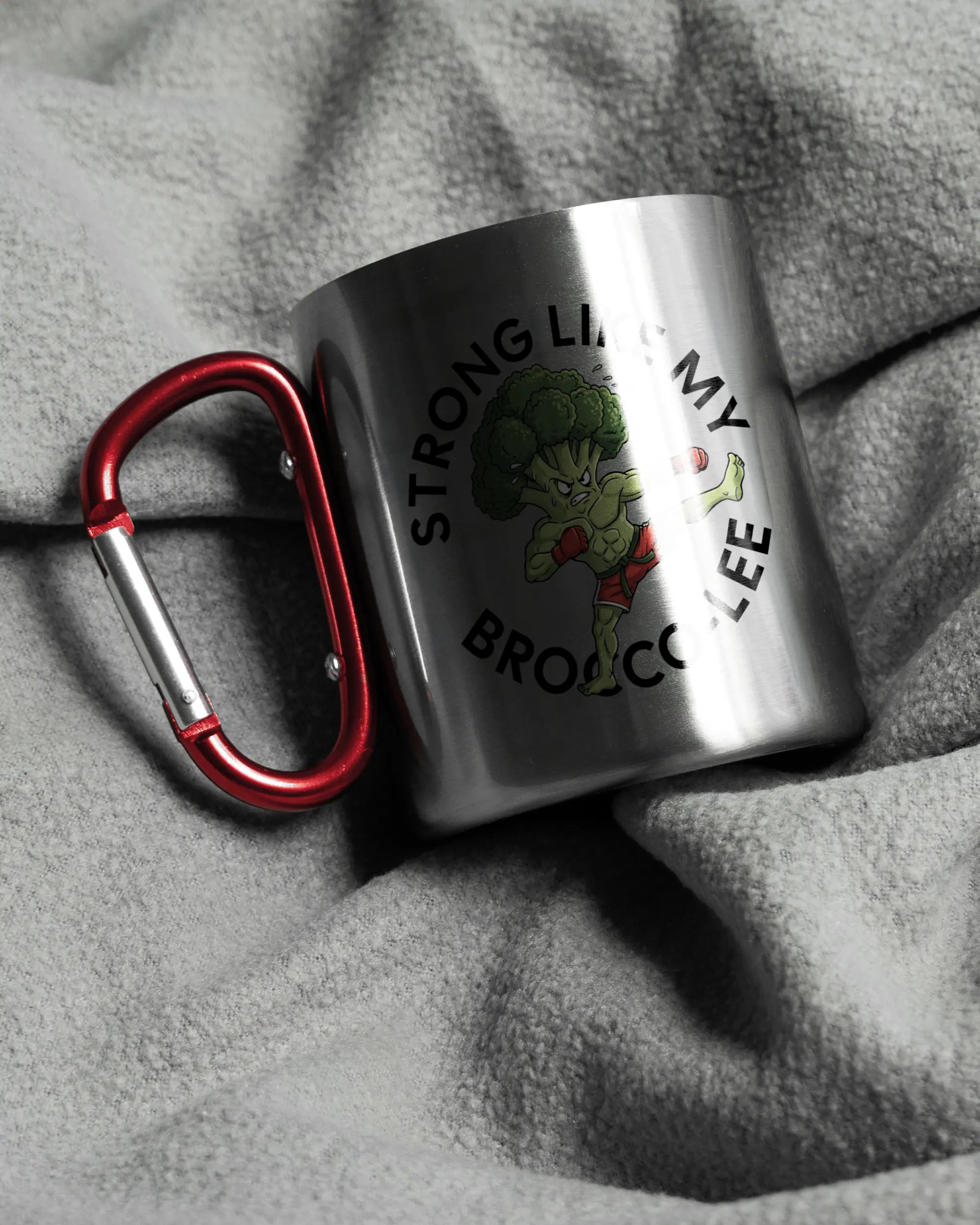 Aufnahme, die die linke Seite der beidseitig bedruckten Edelstahltasse von Maondo auf einer flauschigen Fließdecke mit dem Design Brocco-Lee in der Farbe Metallic-Red zeigt