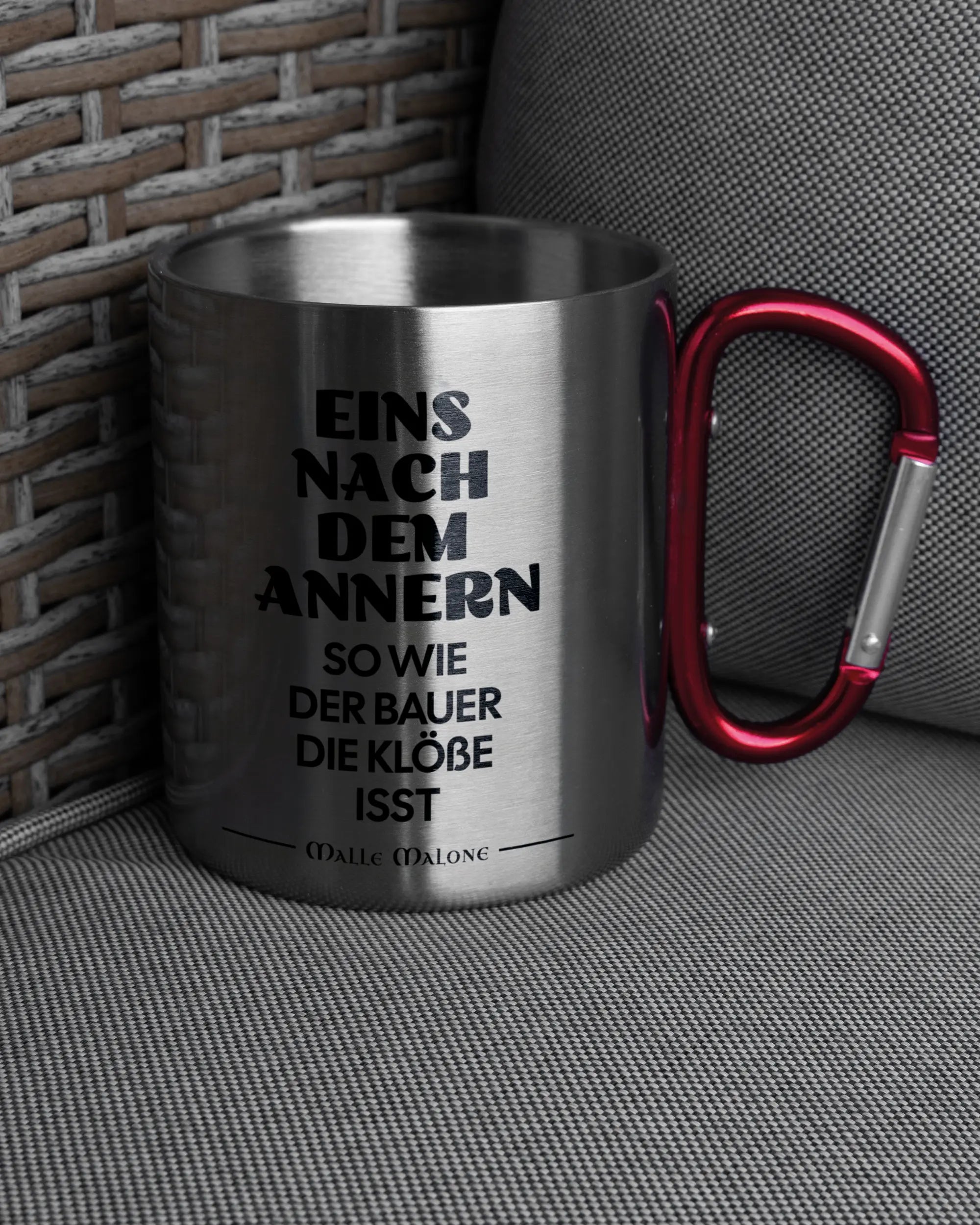 Ansicht der rechten Seite der beidseitig bedruckten Edelstahltasse von Maondo auf einem Balkonmöbel bzw. Campingstuhl mit dem Design Eins nach dem Annern in der Farbe Metallic-Red