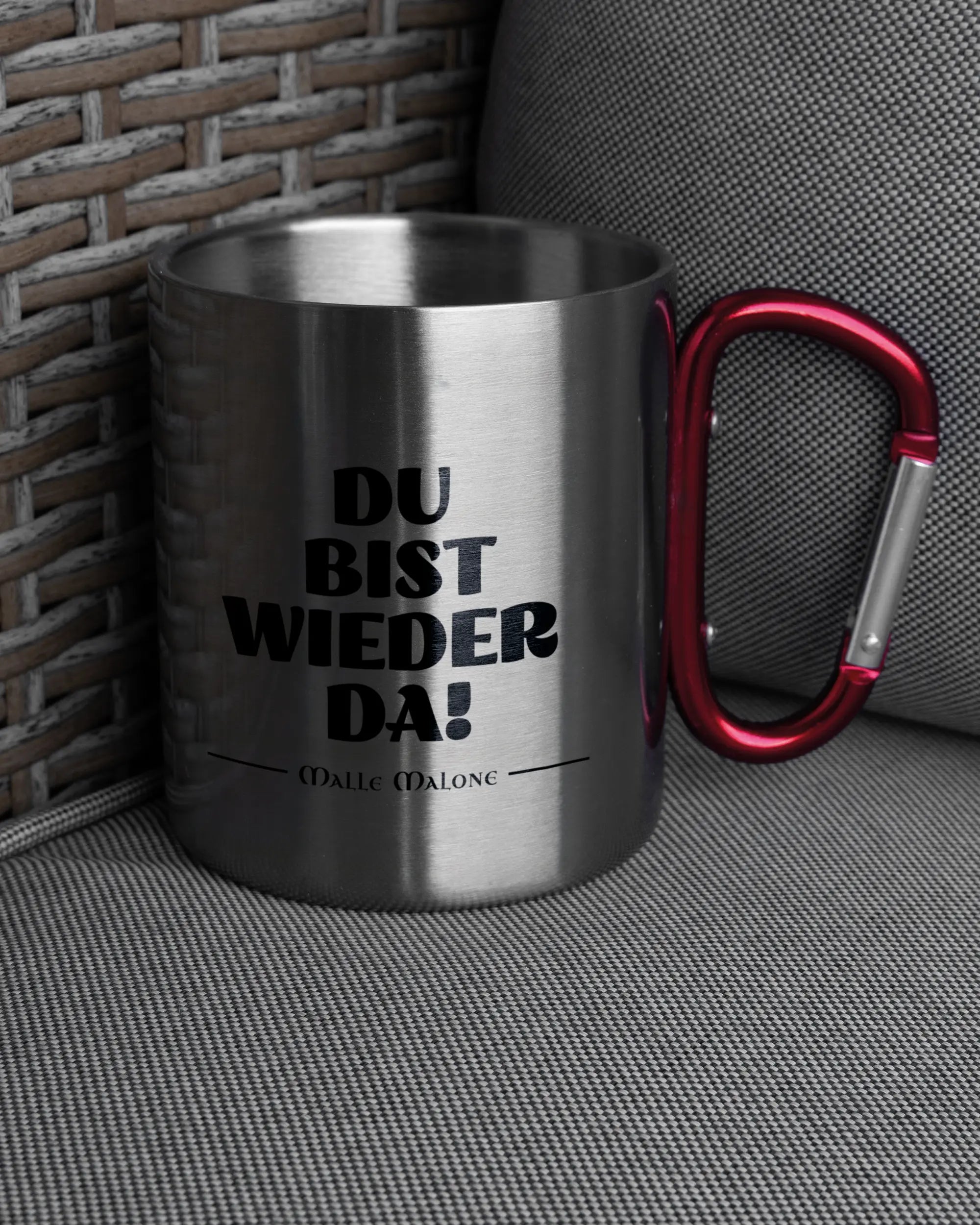 Ansicht der rechten Seite der beidseitig bedruckten Edelstahltasse von Maondo auf einem Balkonmöbel bzw. Campingstuhl mit dem Design Wieder da in der Farbe Metallic-Red