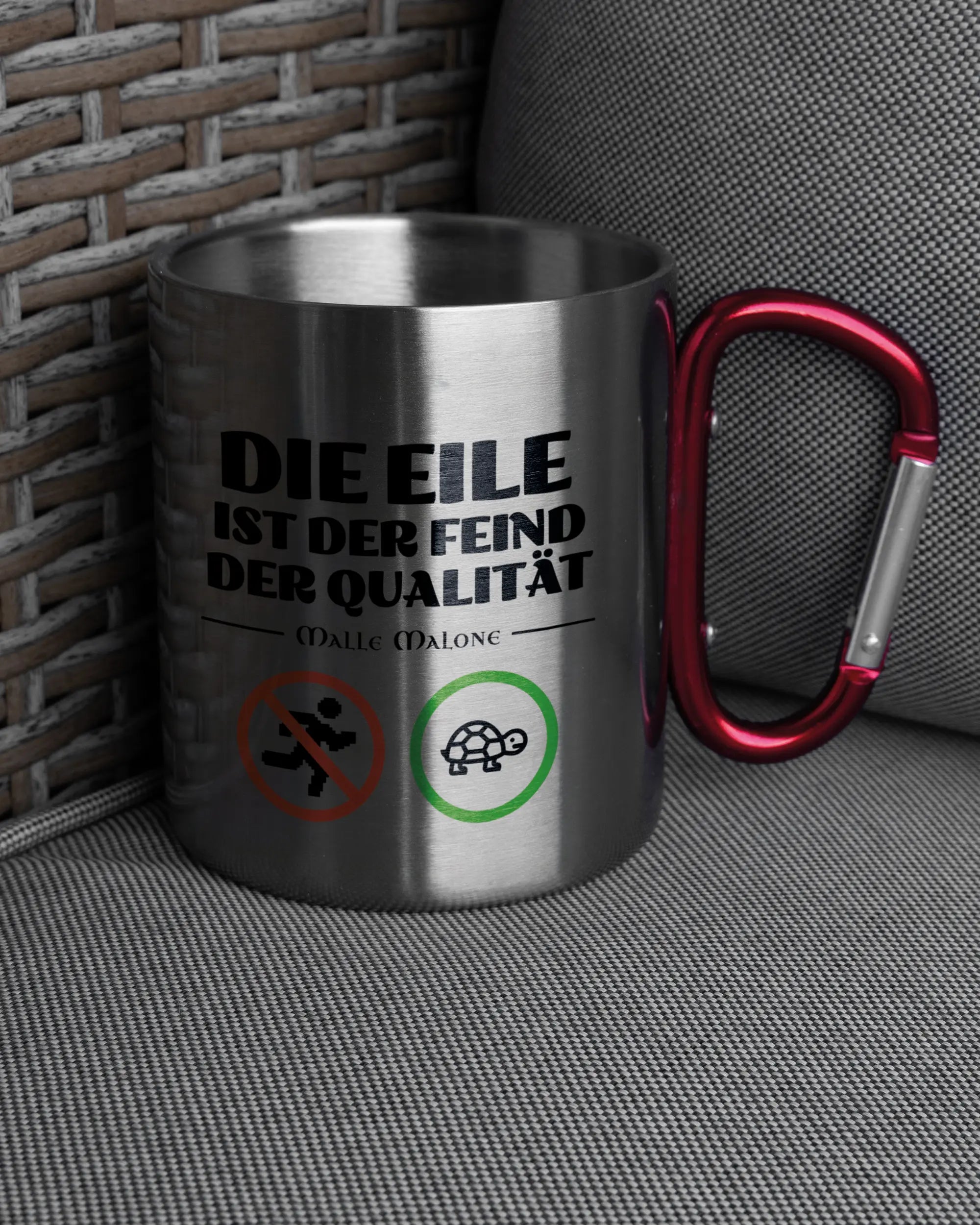 Ansicht der rechten Seite der beidseitig bedruckten Edelstahltasse von Maondo auf einem Balkonmöbel bzw. Campingstuhl mit dem Design Keine Eile in der Farbe Metallic-Red