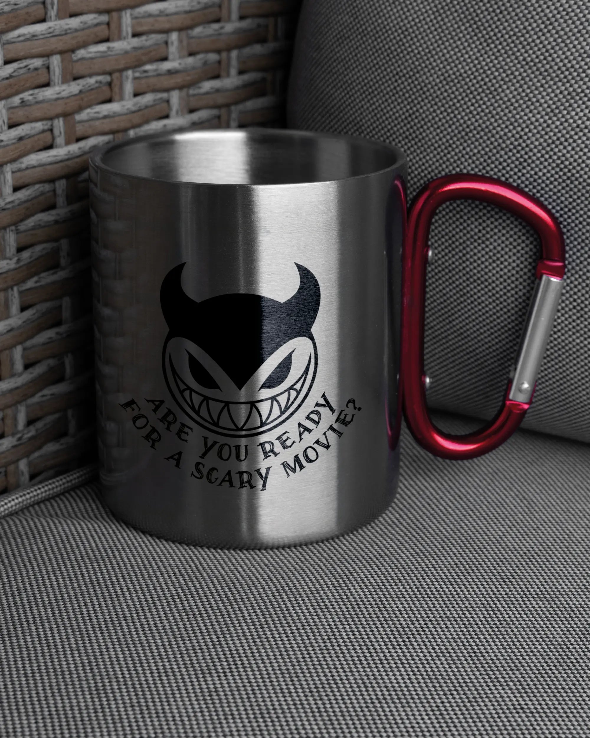 Ansicht der rechten Seite der beidseitig bedruckten Edelstahltasse von Maondo auf einem Balkonmöbel bzw. Campingstuhl mit dem Design Scary Movie in der Farbe Metallic-Red