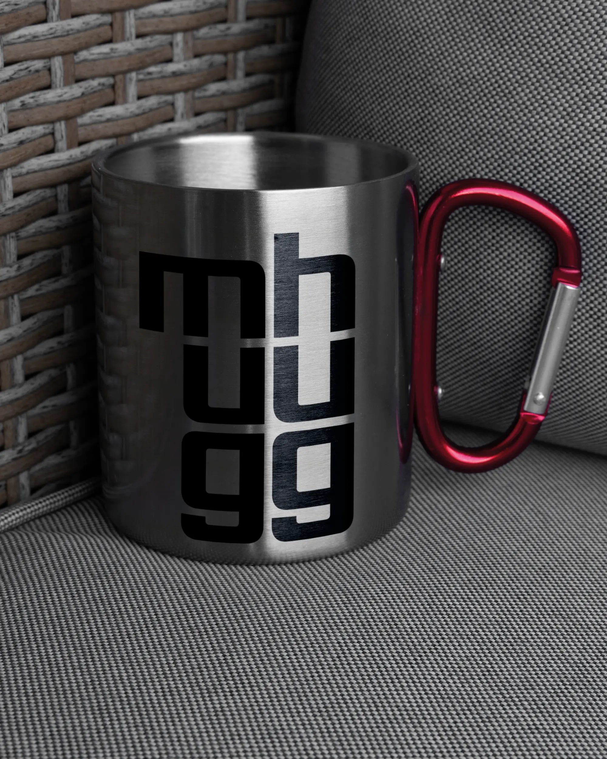 Ansicht der rechten Seite der beidseitig bedruckten Edelstahltasse von Maondo auf einem Balkonmöbel bzw. Campingstuhl mit dem Design Hug Mug in der Farbe Metallic-Red