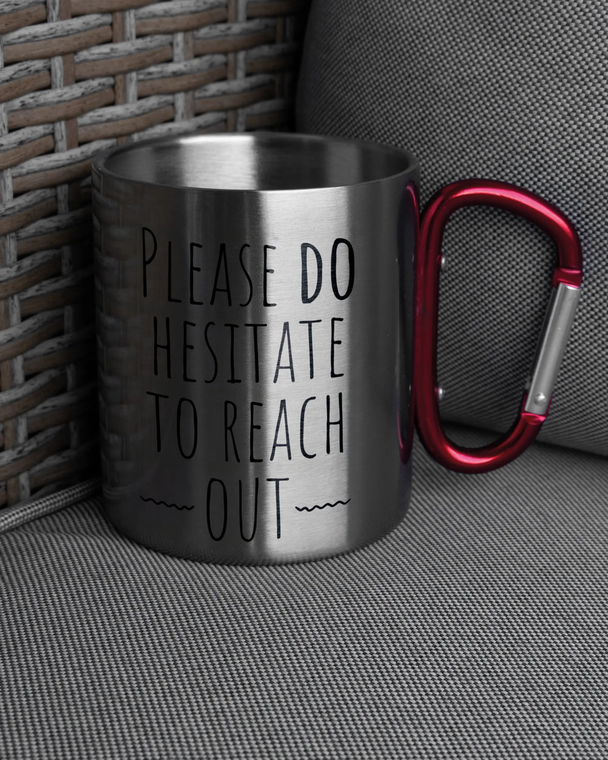 Ansicht der rechten Seite der beidseitig bedruckten Edelstahltasse von Maondo auf einem Balkonmöbel bzw. Campingstuhl mit dem Design Please Hesitate in der Farbe Metallic-Red