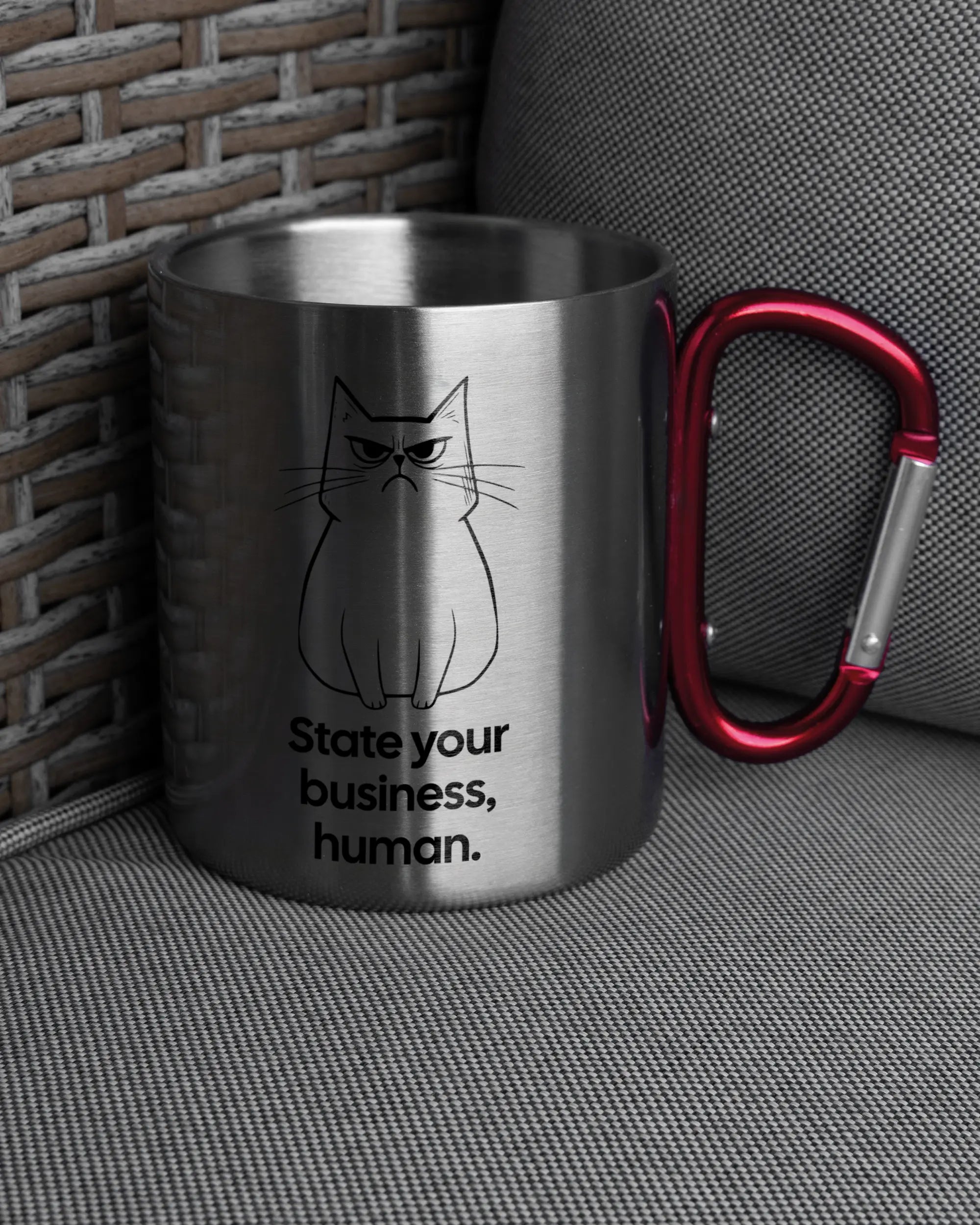 Ansicht der rechten Seite der beidseitig bedruckten Edelstahltasse von Maondo auf einem Balkonmöbel bzw. Campingstuhl mit dem Design Grumpy Purr in der Farbe Metallic-Red