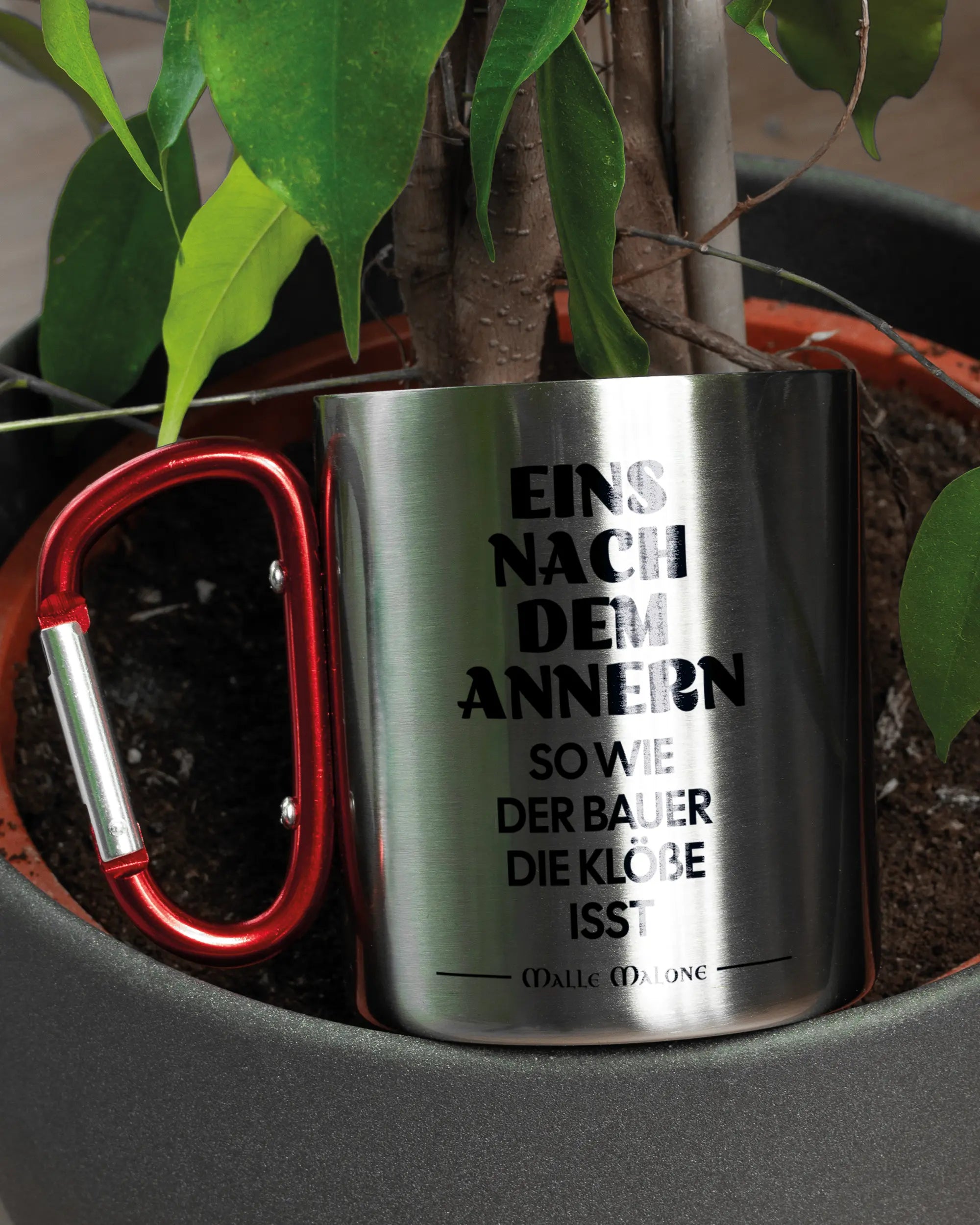 Aufnahme der linken Seite der beidseitig bedruckten Edelstahltasse von Maondo mit dem Design Eins nach dem Annern in der Farbe Metallic-Red in einem Blumentopf