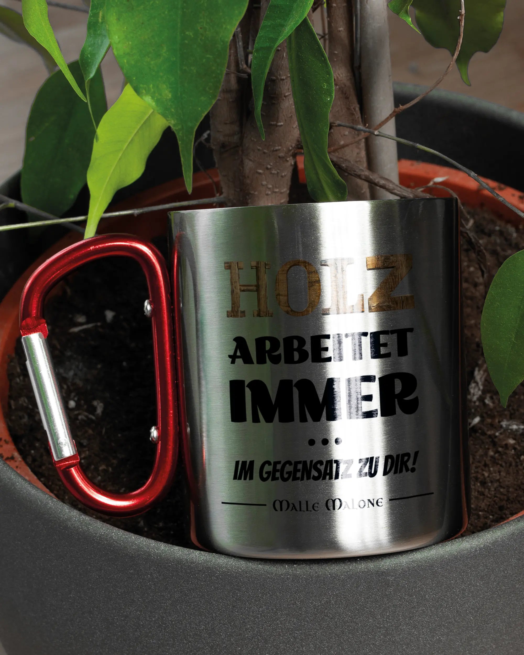 Aufnahme der linken Seite der beidseitig bedruckten Edelstahltasse von Maondo mit dem Design Holzarbeit in der Farbe Metallic-Red in einem Blumentopf