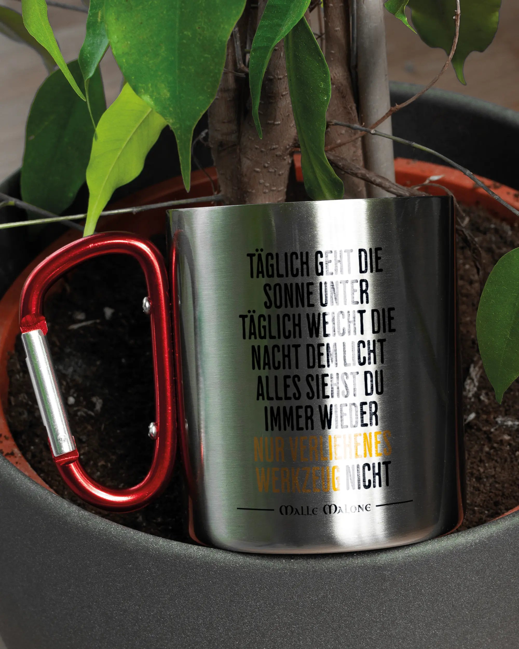 Aufnahme der linken Seite der beidseitig bedruckten Edelstahltasse von Maondo mit dem Design Wegzeug in der Farbe Metallic-Red in einem Blumentopf
