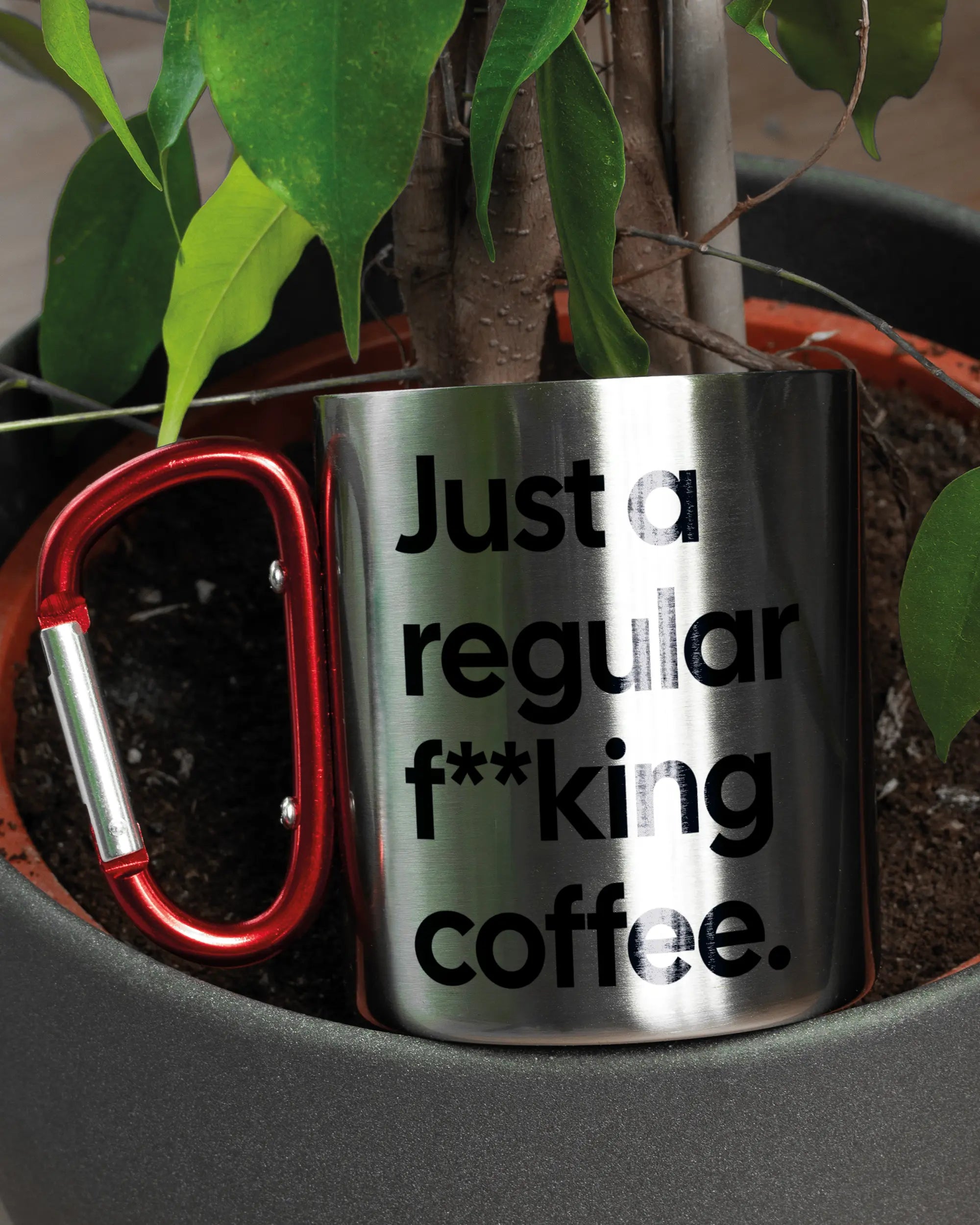 Aufnahme der linken Seite der beidseitig bedruckten Edelstahltasse von Maondo mit dem Design Regular Coffee in der Farbe Metallic-Red in einem Blumentopf