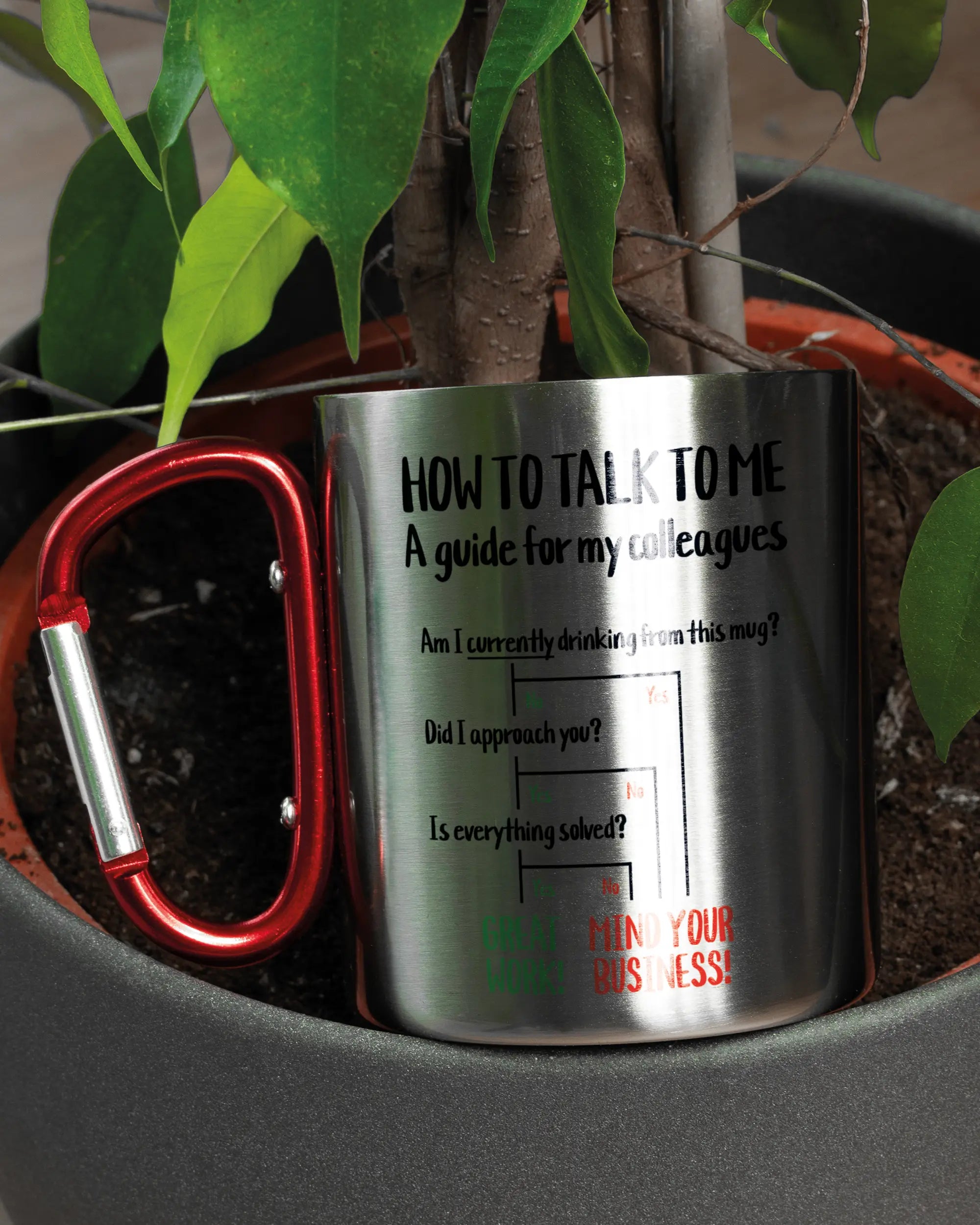 Aufnahme der linken Seite der beidseitig bedruckten Edelstahltasse von Maondo mit dem Design Colleagues Guide in der Farbe Metallic-Red in einem Blumentopf