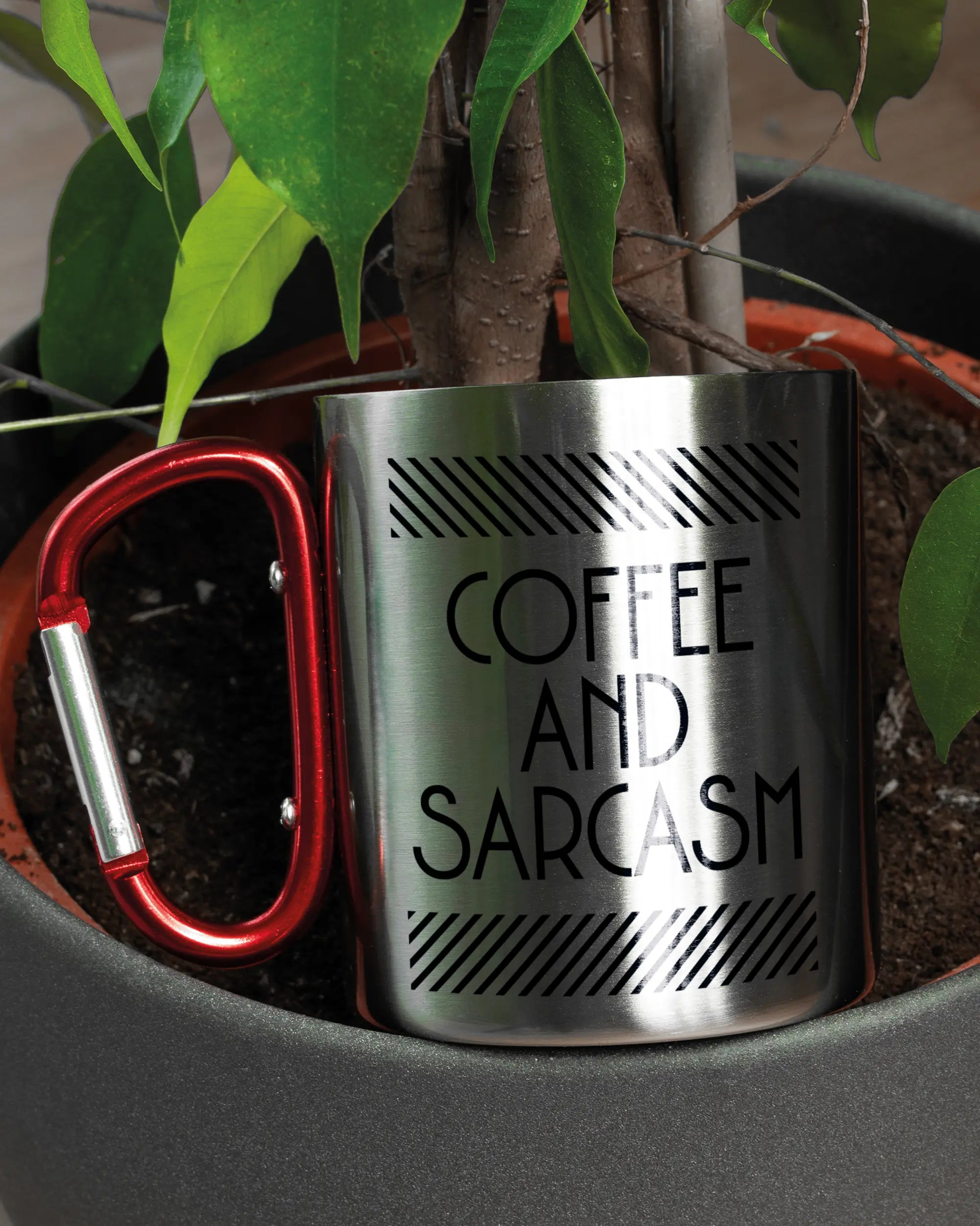 Aufnahme der linken Seite der beidseitig bedruckten Edelstahltasse von Maondo mit dem Design Sarcastic Cup in der Farbe Metallic-Red in einem Blumentopf