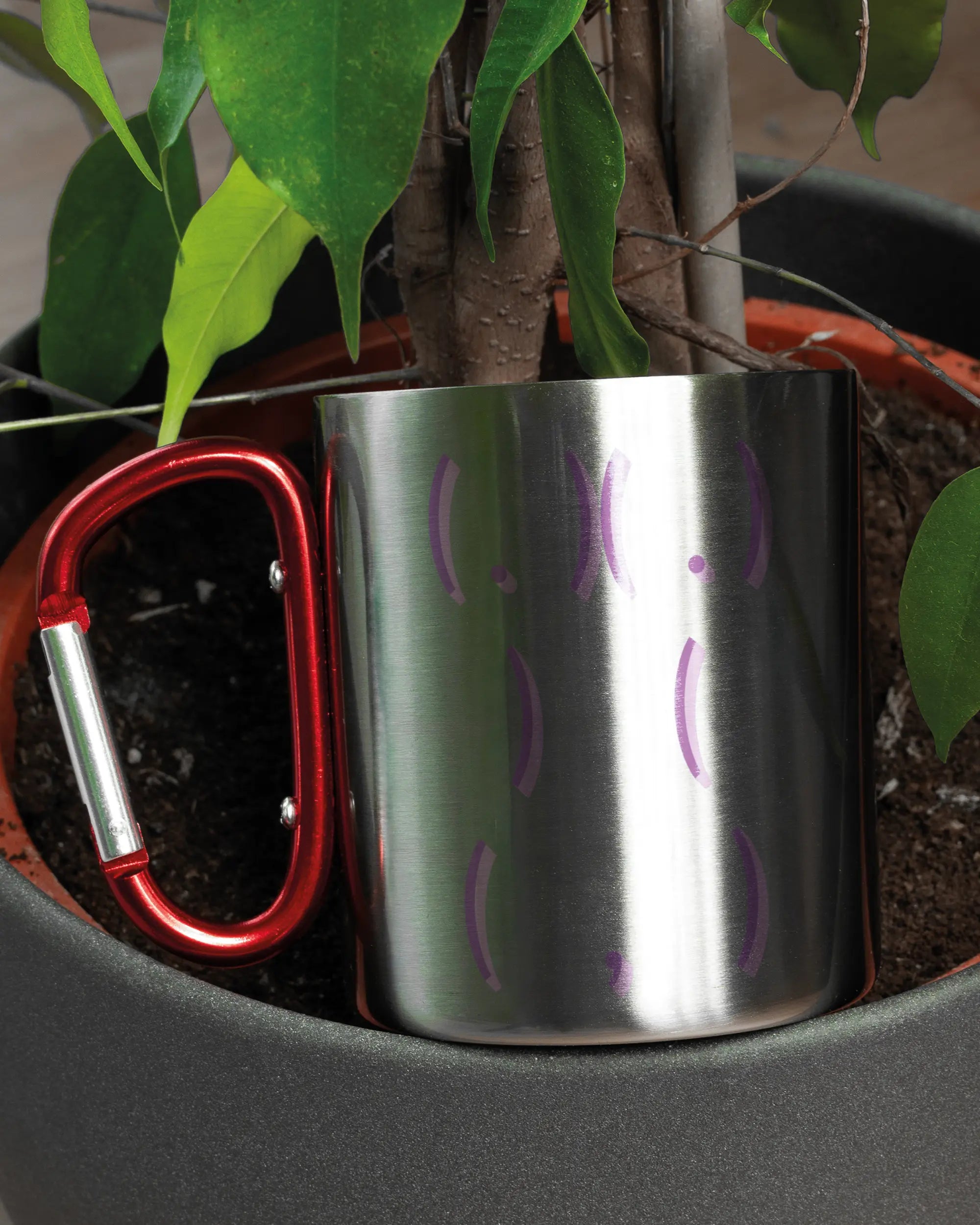 Aufnahme der linken Seite der beidseitig bedruckten Edelstahltasse von Maondo mit dem Design Body Language in der Farbe Metallic-Red in einem Blumentopf