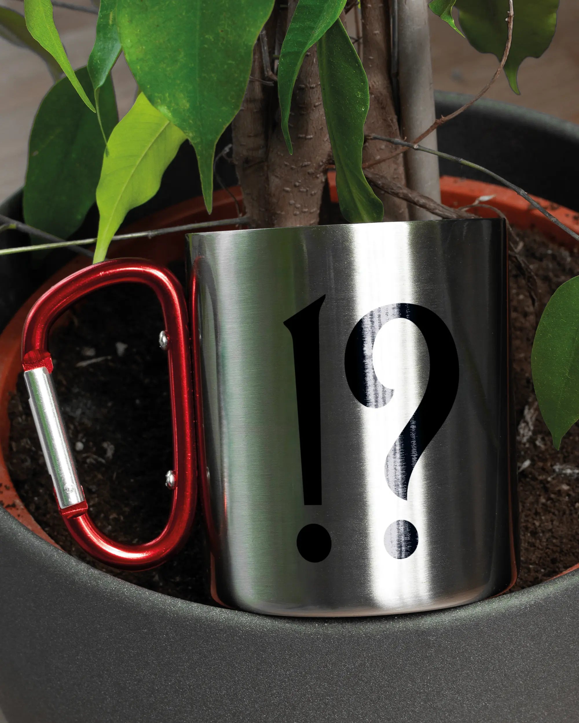 Aufnahme der linken Seite der beidseitig bedruckten Edelstahltasse von Maondo mit dem Design WHAT in der Farbe Metallic-Red in einem Blumentopf