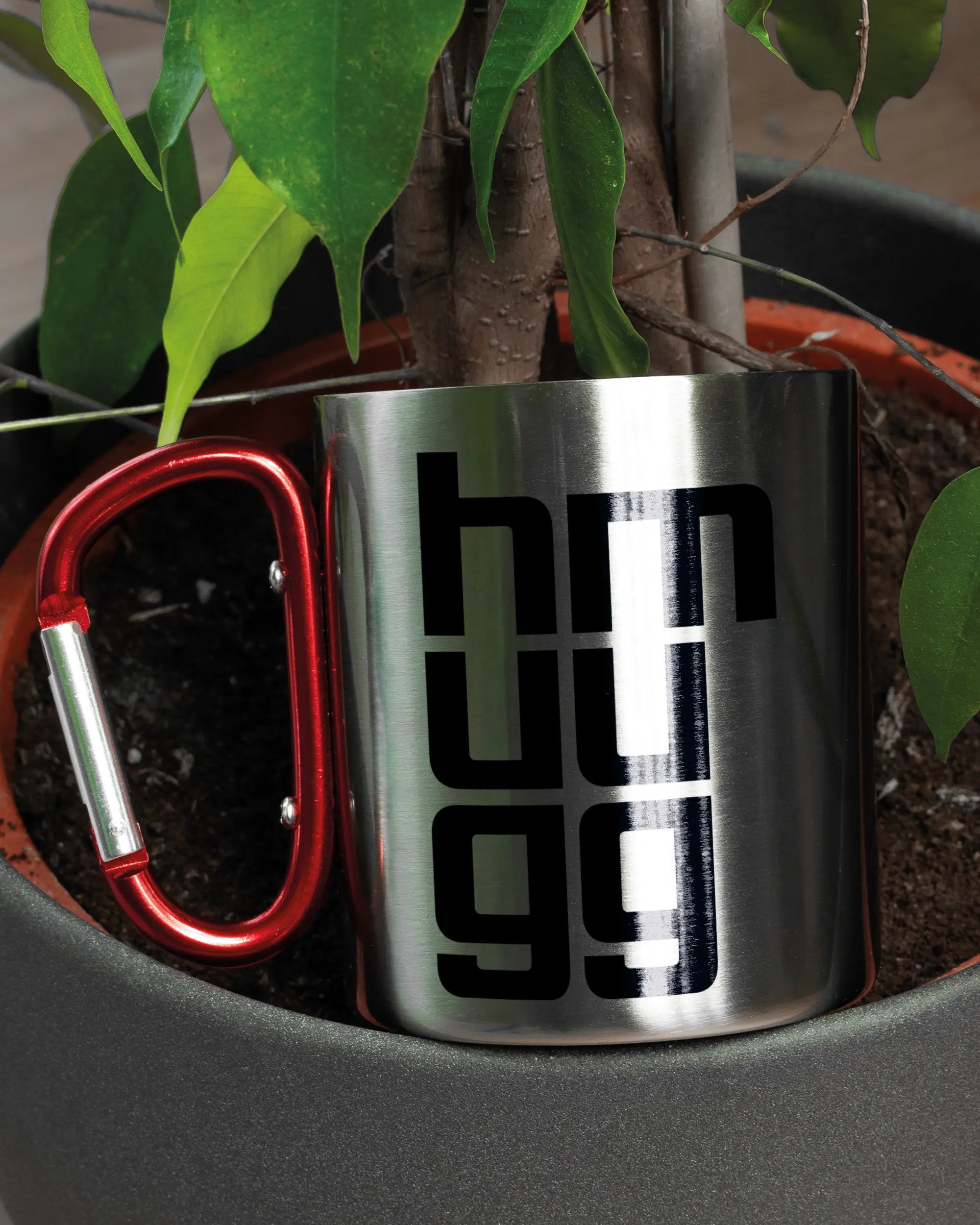 Aufnahme der linken Seite der beidseitig bedruckten Edelstahltasse von Maondo mit dem Design Hug Mug in der Farbe Metallic-Red in einem Blumentopf