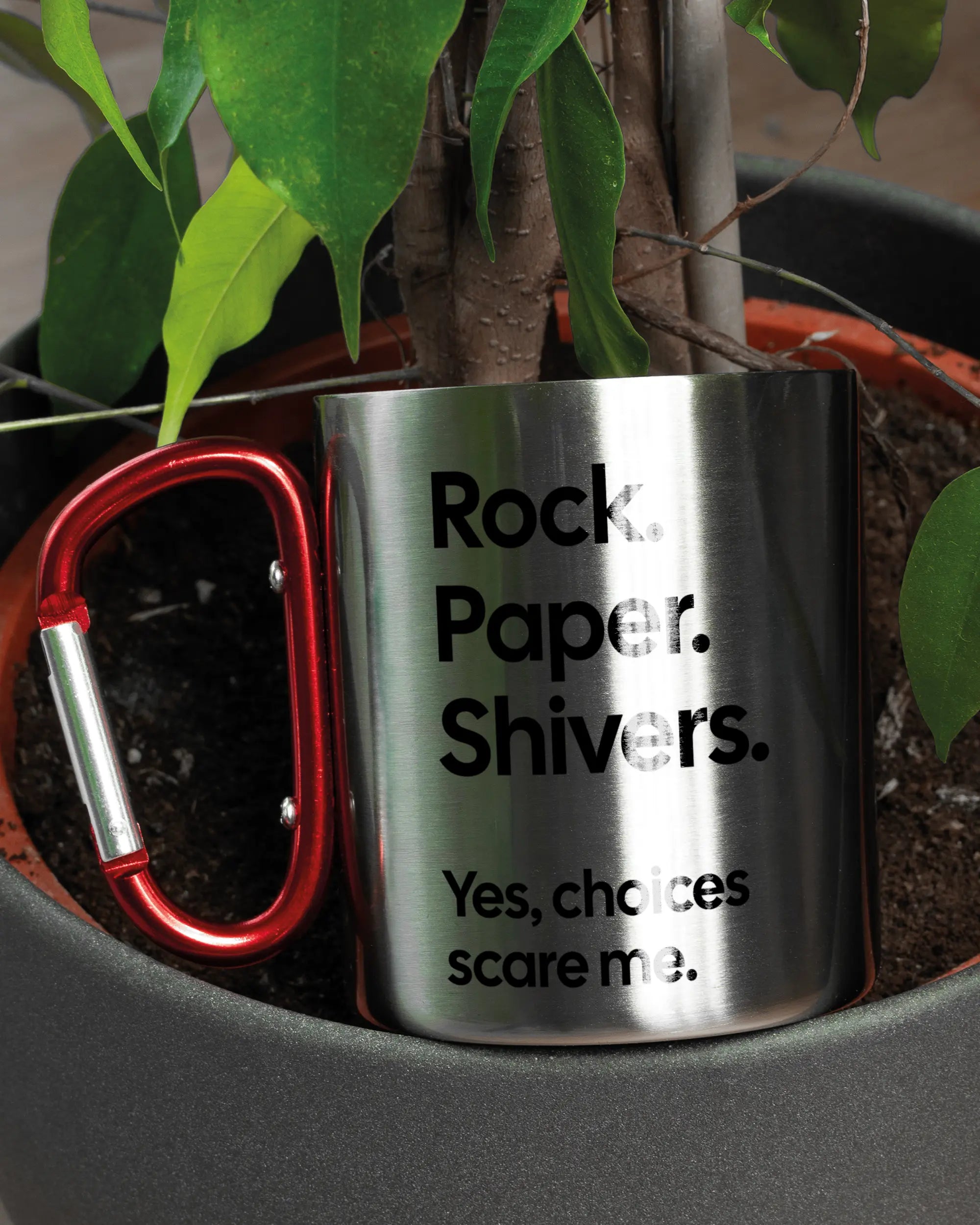 Aufnahme der linken Seite der beidseitig bedruckten Edelstahltasse von Maondo mit dem Design Rock Paper Shivers in der Farbe Metallic-Red in einem Blumentopf