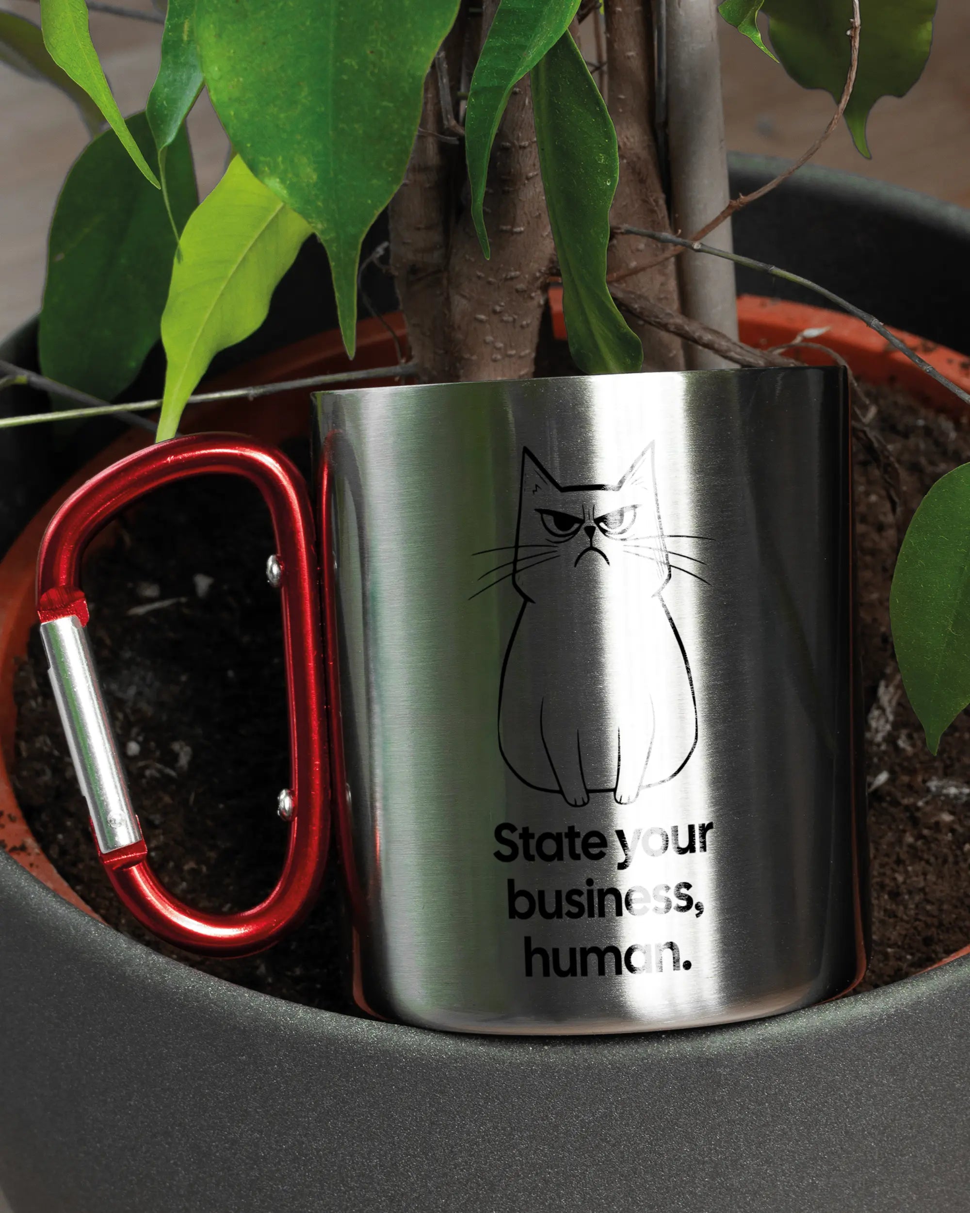 Aufnahme der linken Seite der beidseitig bedruckten Edelstahltasse von Maondo mit dem Design Grumpy Purr in der Farbe Metallic-Red in einem Blumentopf