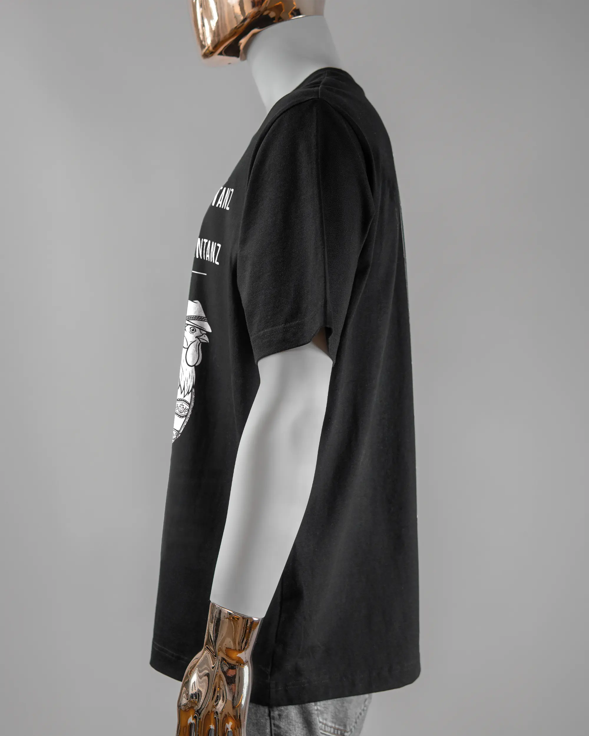 Seitenansicht des Organic Unisex T-Shirt Heavy Oversized von Maondo mit dem Design Trachtentanz vorne in der Farbe Black und in der Größe L getragen von einer maskulinen Puppe