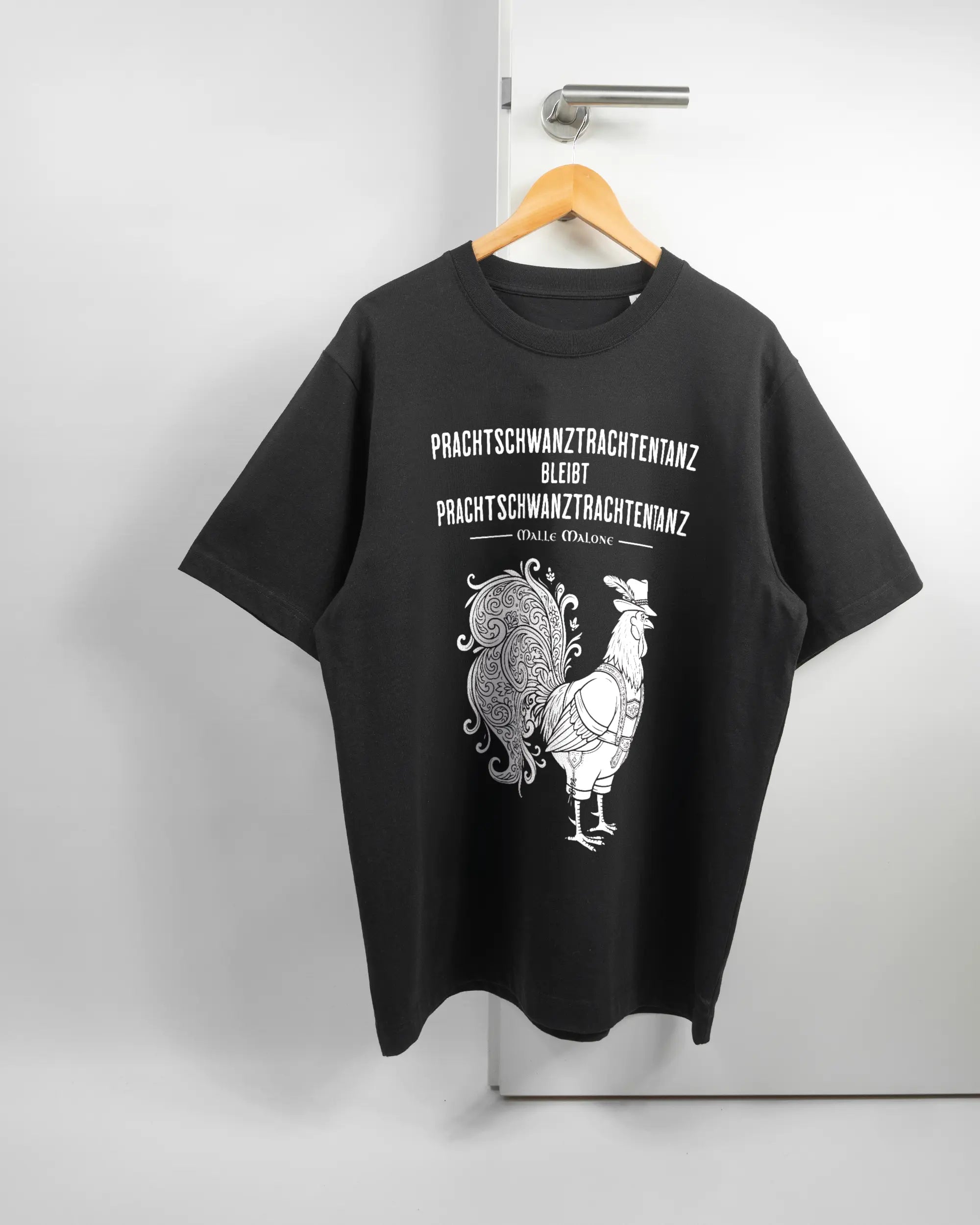 Vorderseite des Organic Unisex T-Shirt Heavy Oversized von Maondo mit dem Design Trachtentanz in der Farbe Black und in der Größe L auf einem Bügel an der Türklinke aufgehängt