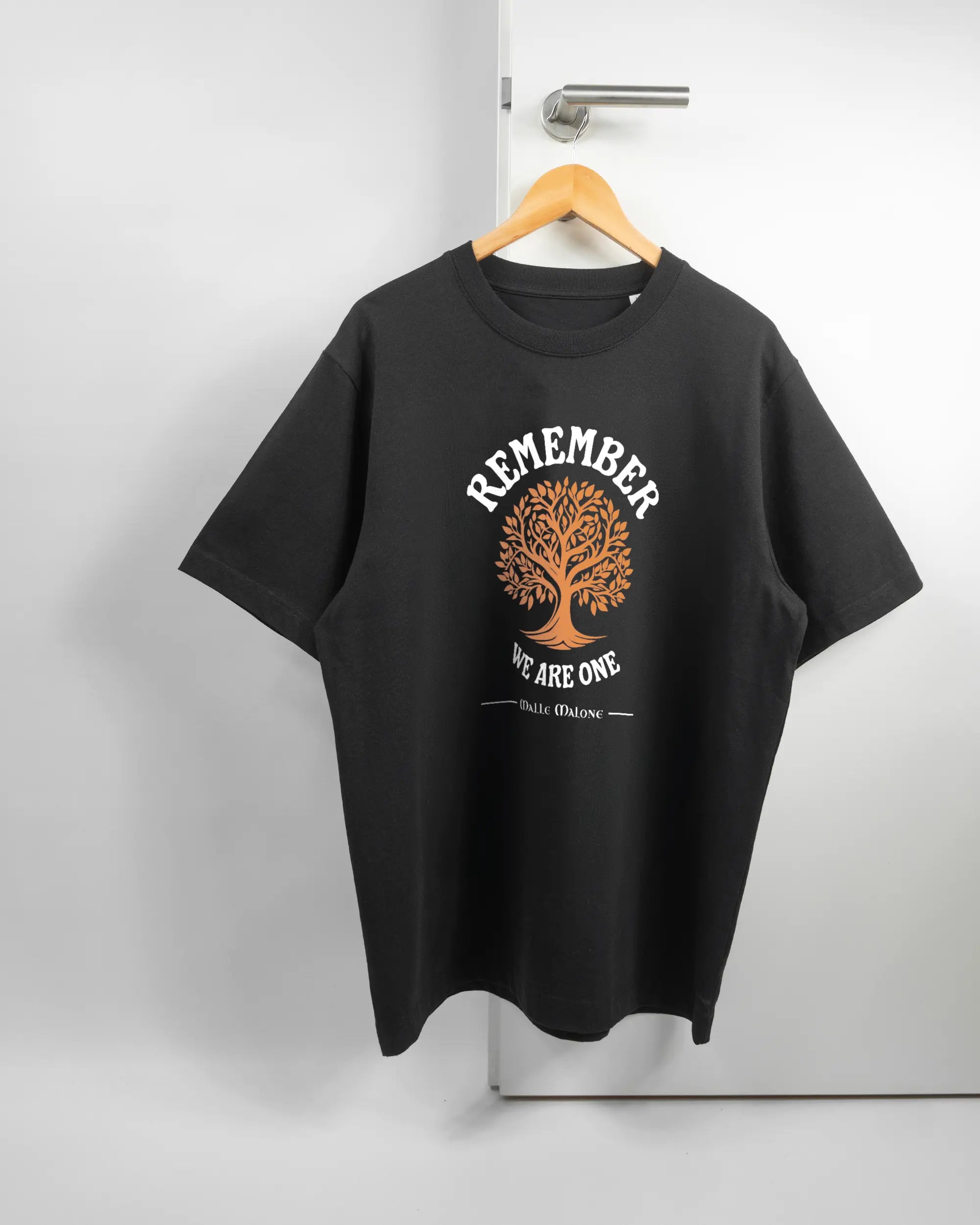 Vorderseite des Organic Unisex T-Shirt Heavy Oversized von Maondo mit dem Design We are one in der Farbe Black und in der Größe L auf einem Bügel an der Türklinke aufgehängt