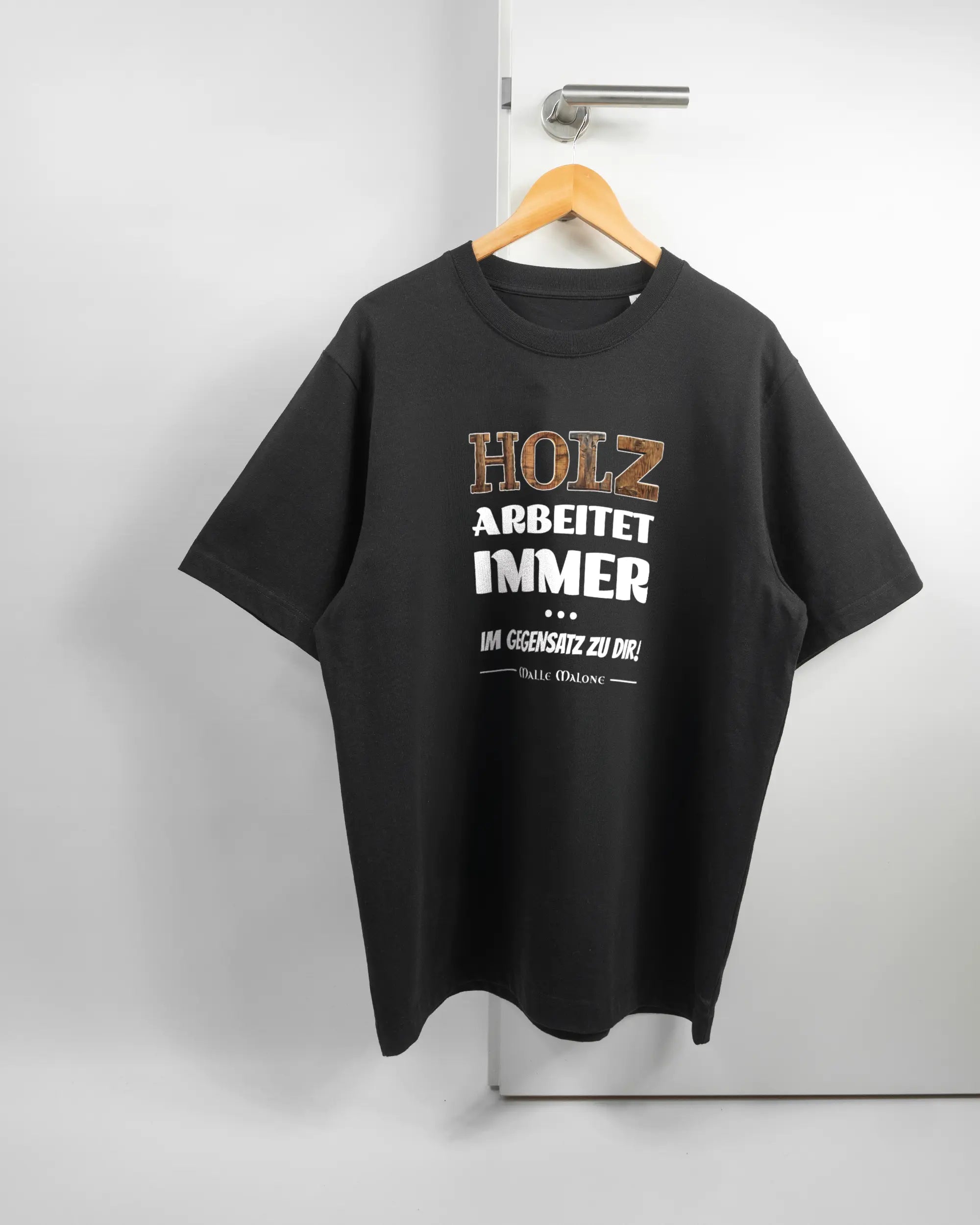 Vorderseite des Organic Unisex T-Shirt Heavy Oversized von Maondo mit dem Design Holzarbeit in der Farbe Black und in der Größe L auf einem Bügel an der Türklinke aufgehängt