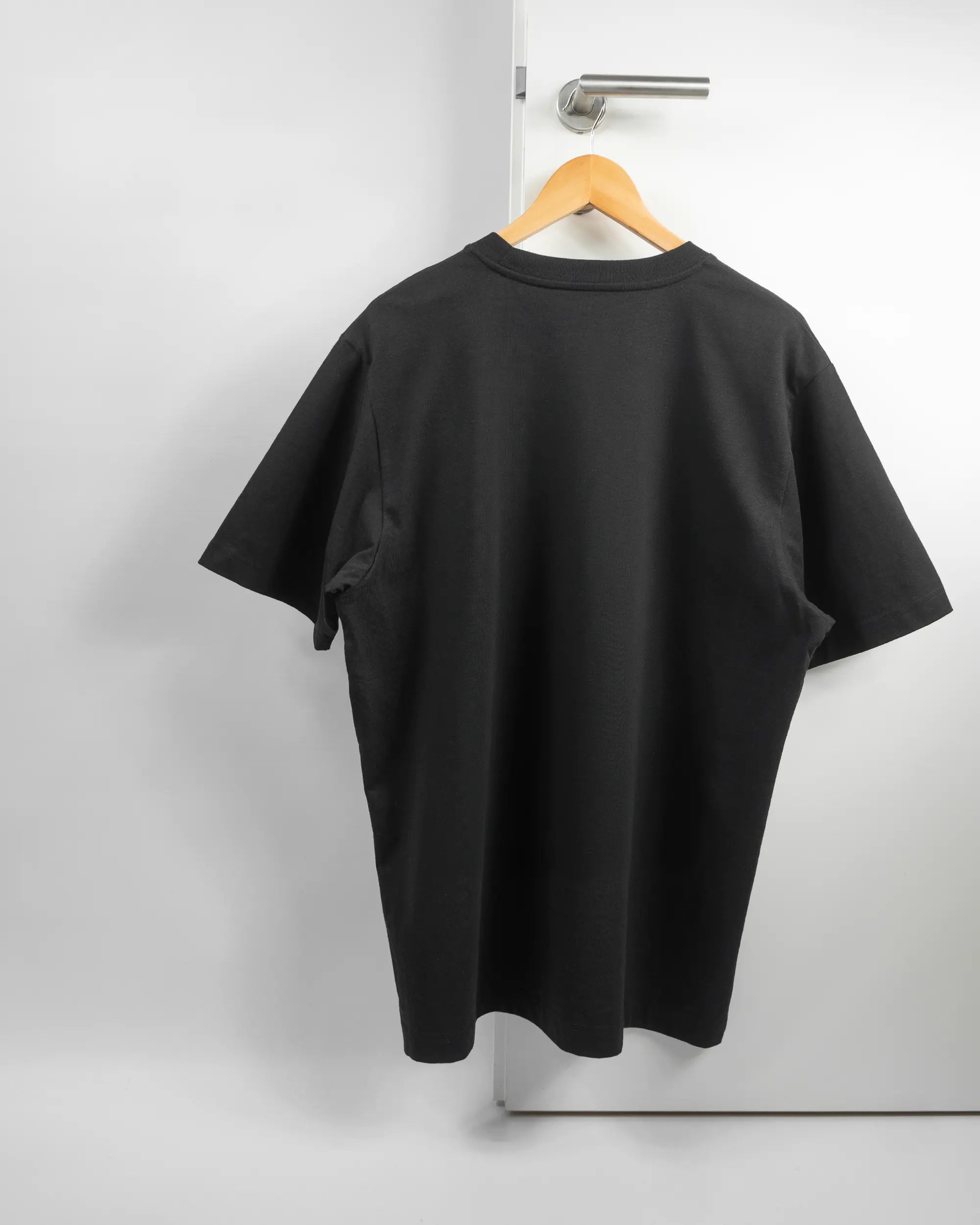 Rückseite des Organic Unisex T-Shirt Heavy Oversized von Maondo ohne Motiv in der Farbe Black und in der Größe L auf einem Bügel an der Türklinke aufgehängt